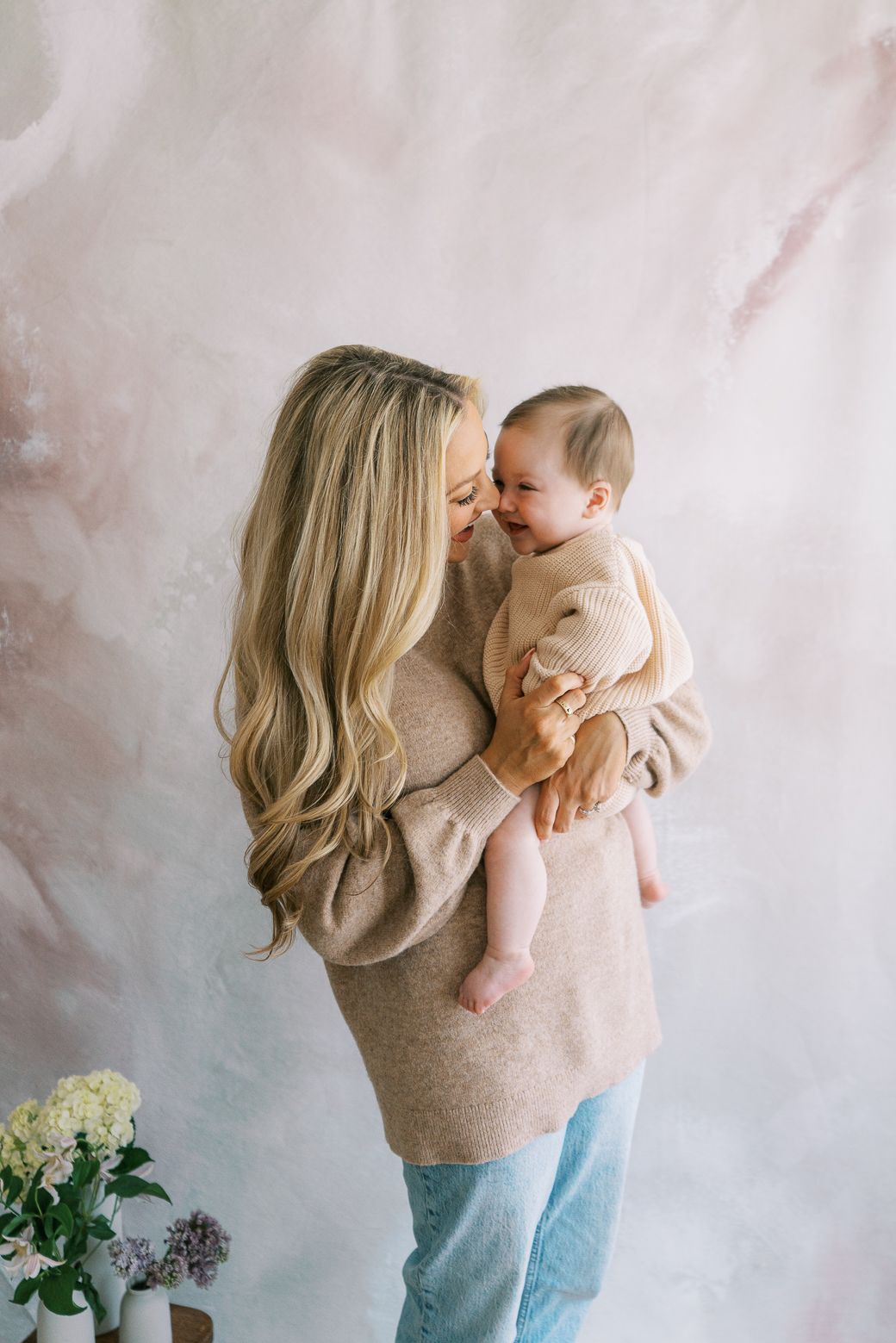 Sweet candid moments between parent and baby against soft pastel background with hydrangeas.