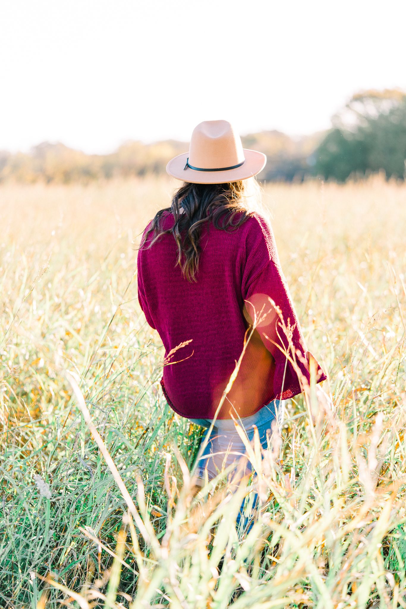 Dreamy outdoor photoshoot in a burgundy sweater and hat among tall wheat fields at golden hour.