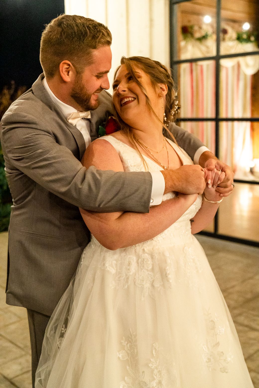 A romantic wedding couple shares an intimate dance together in a sunlit venue with large windows.
