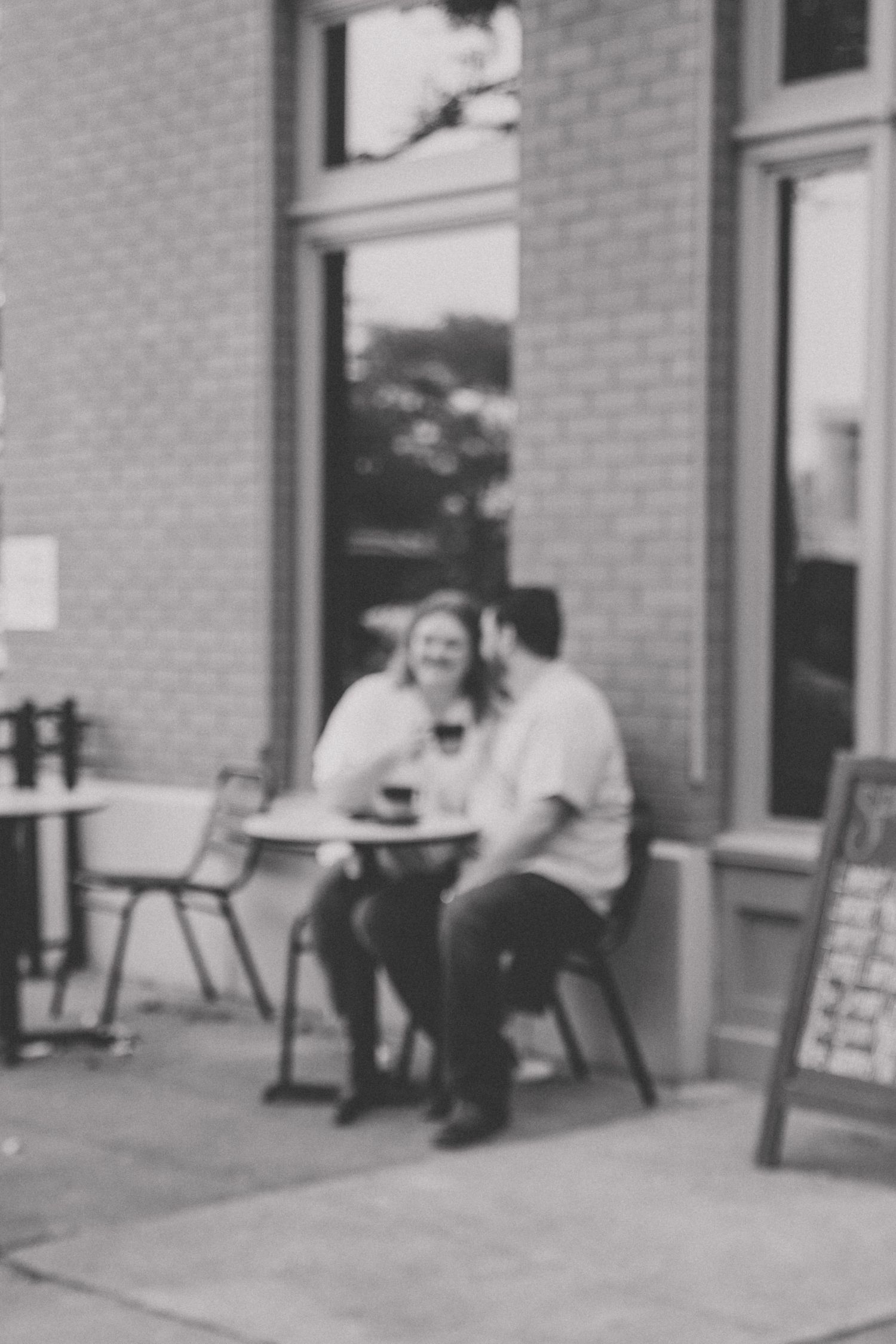 A black and white photo of a couple sitting together at an outdoor cafe, laughing and enjoying coffee.