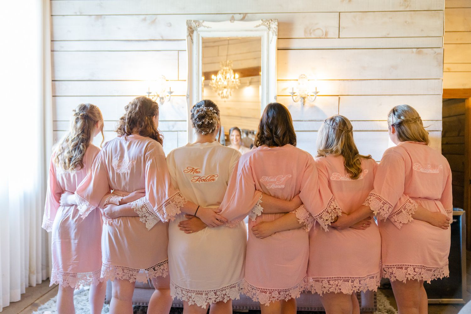 Row of bridesmaids in matching pink robes standing with their backs to camera.