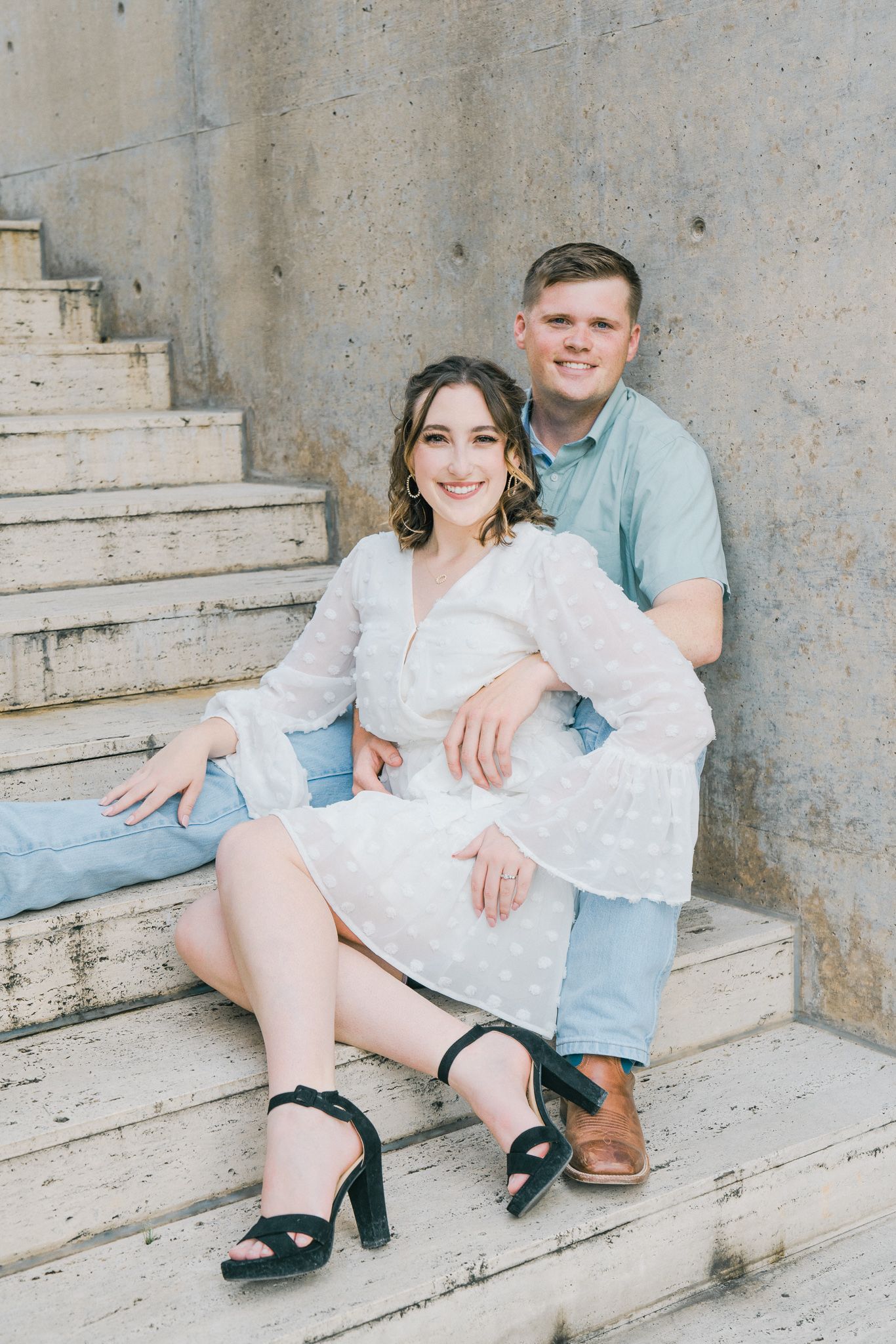 Couple sits casually on concrete steps during outdoor photo session with vintage architectural backdrop.