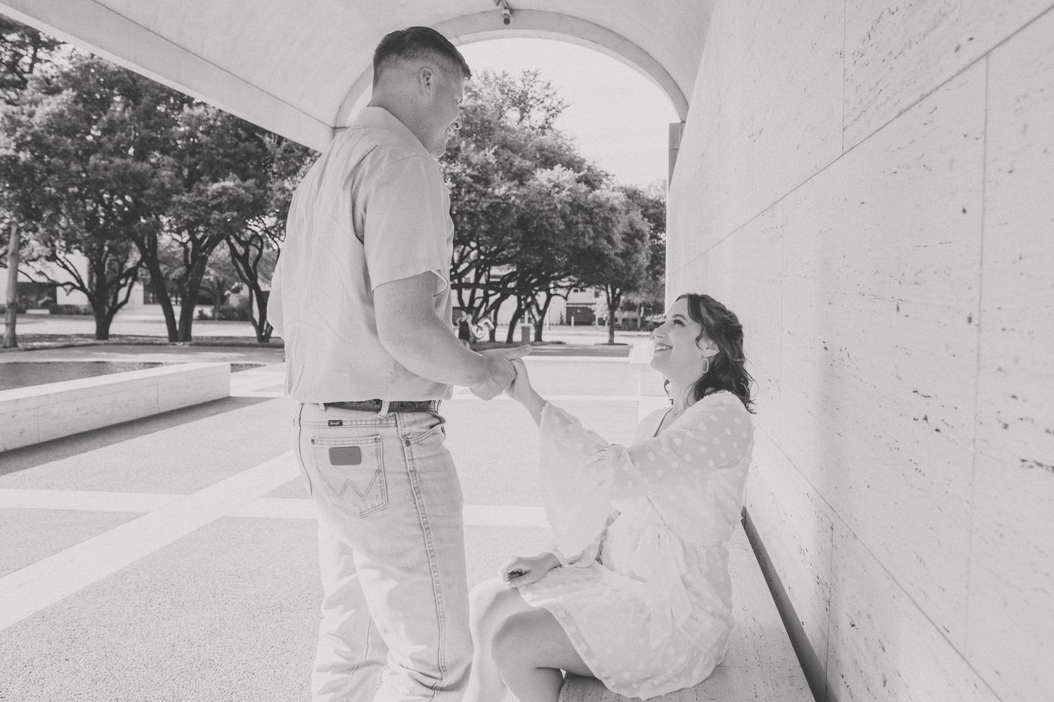 A black and white photo of two people sharing a tender moment under an arched walkway.