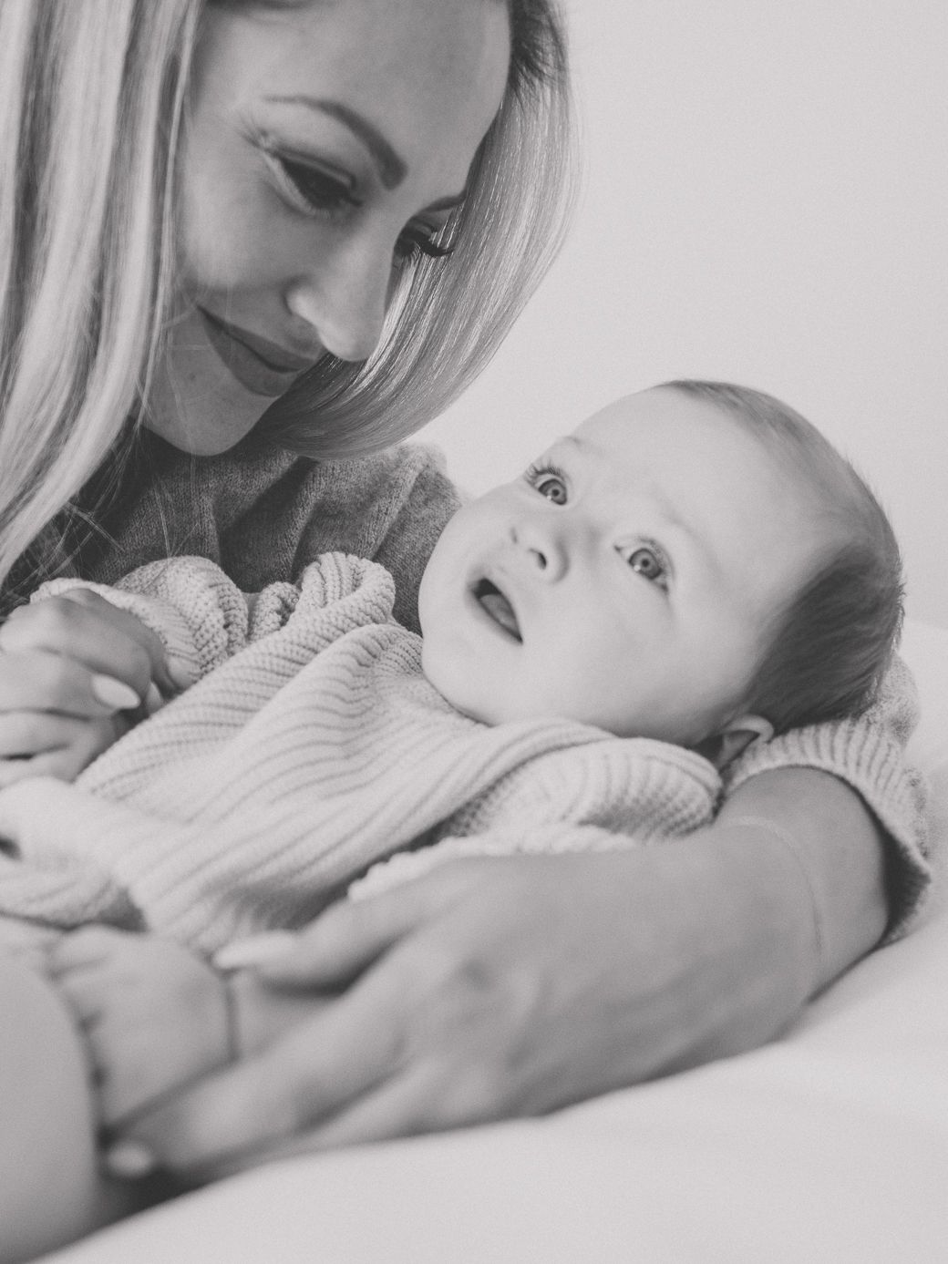 Black and white portraits capturing gentle interactions between caregiver and baby in natural light.