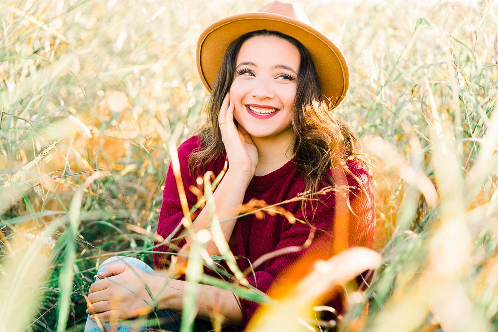 Person wearing red sweater and brown hat sits in golden autumn field.