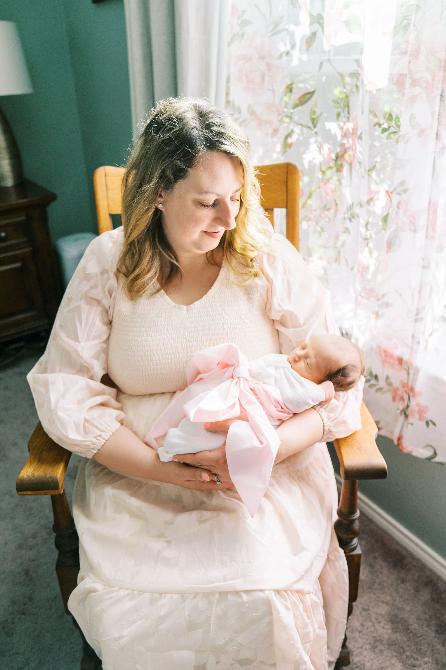 A parent cradles a newborn baby in soft pink clothing near a sunlit window.