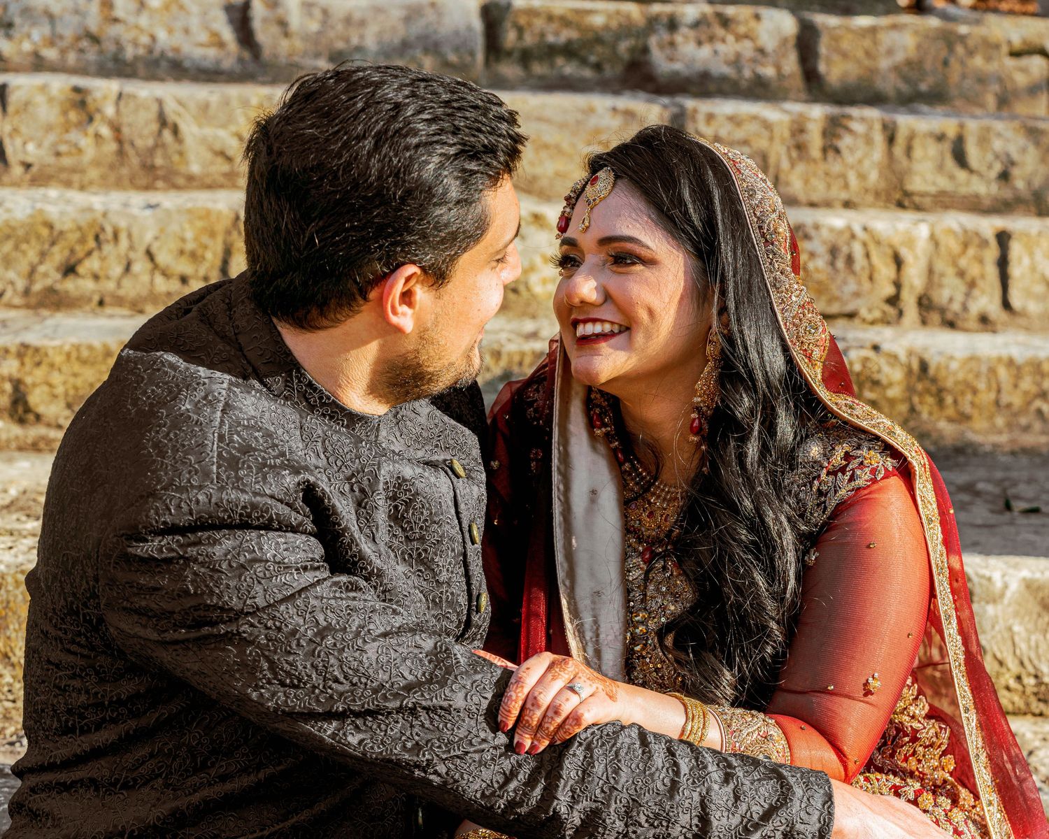 A couple shares a joyful moment against a stone wall during their wedding celebration.