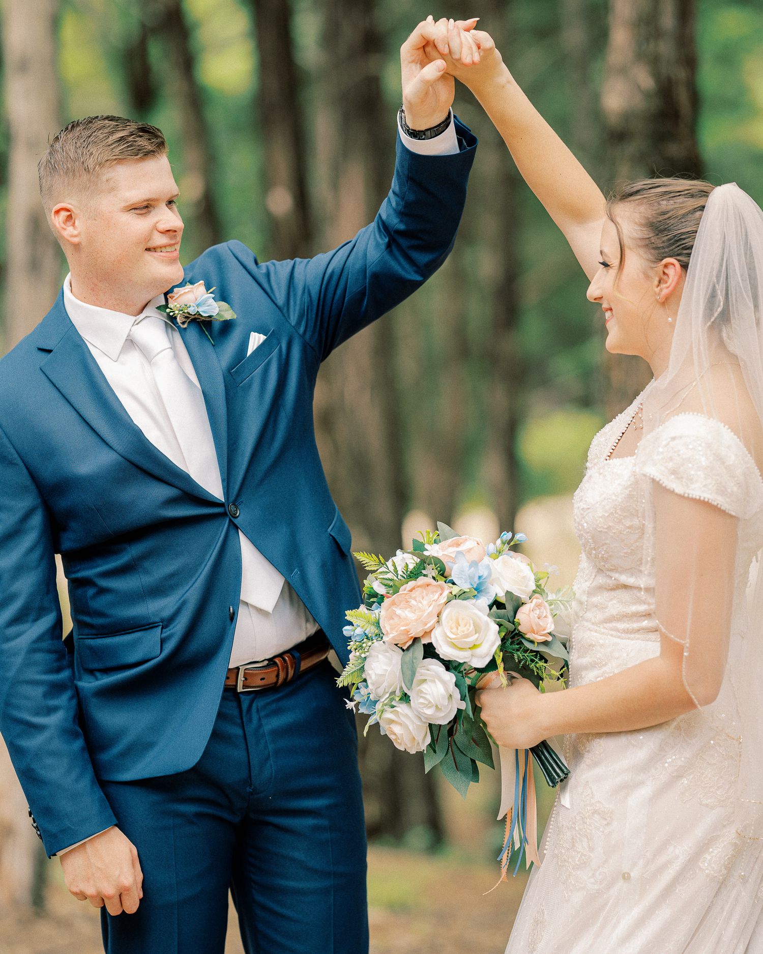 Bride and groom celebrate with raised arms while dancing together in a wooded outdoor setting.