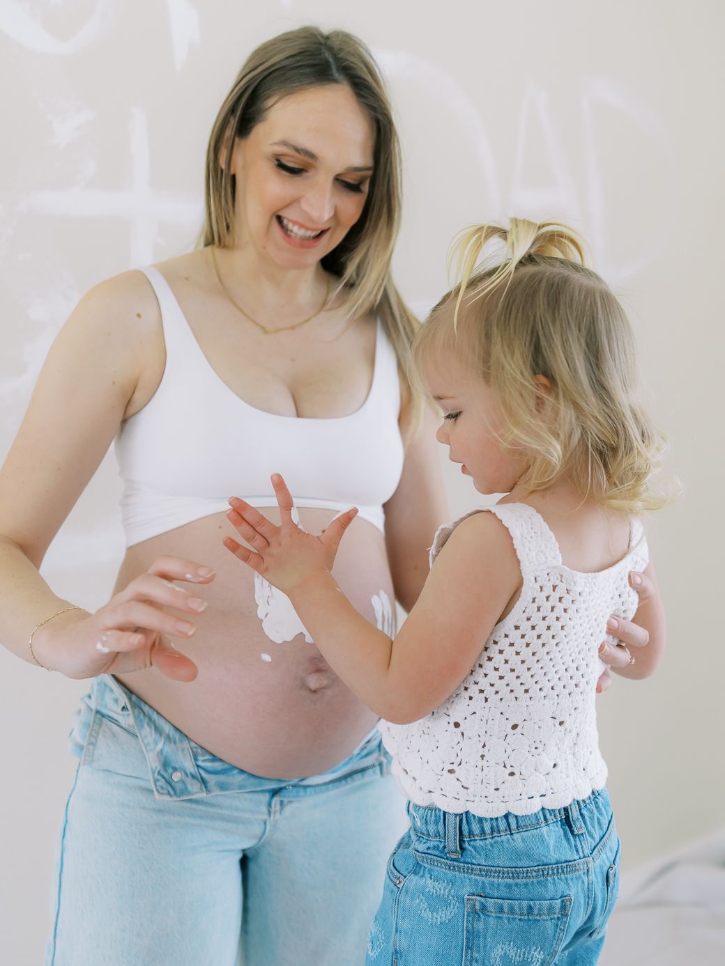 Mother and daughter in matching white tops and denim share playful moment together.