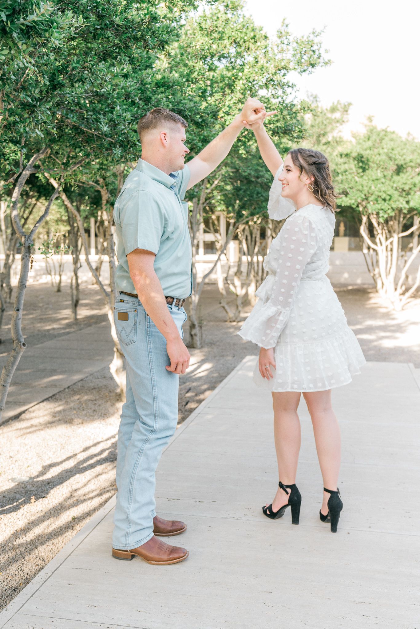 A romantic outdoor photoshoot showing playful interaction between a couple in light summer attire.