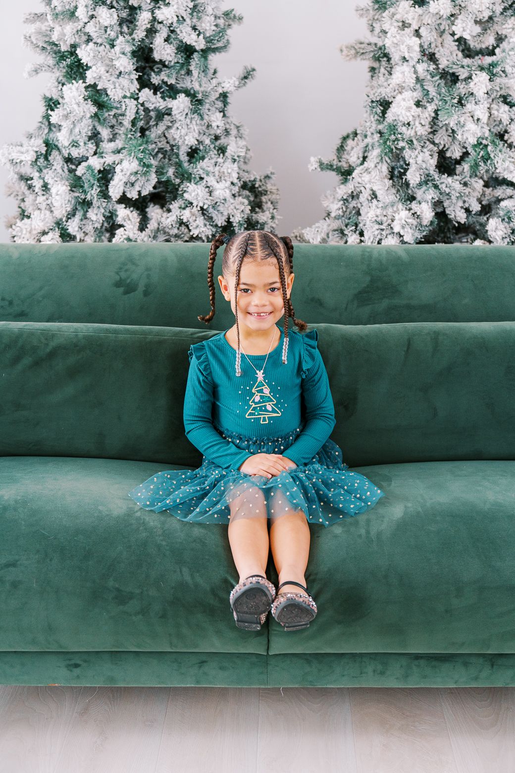 A festive holiday scene with a green velvet couch and snow-flocked Christmas trees in the background.