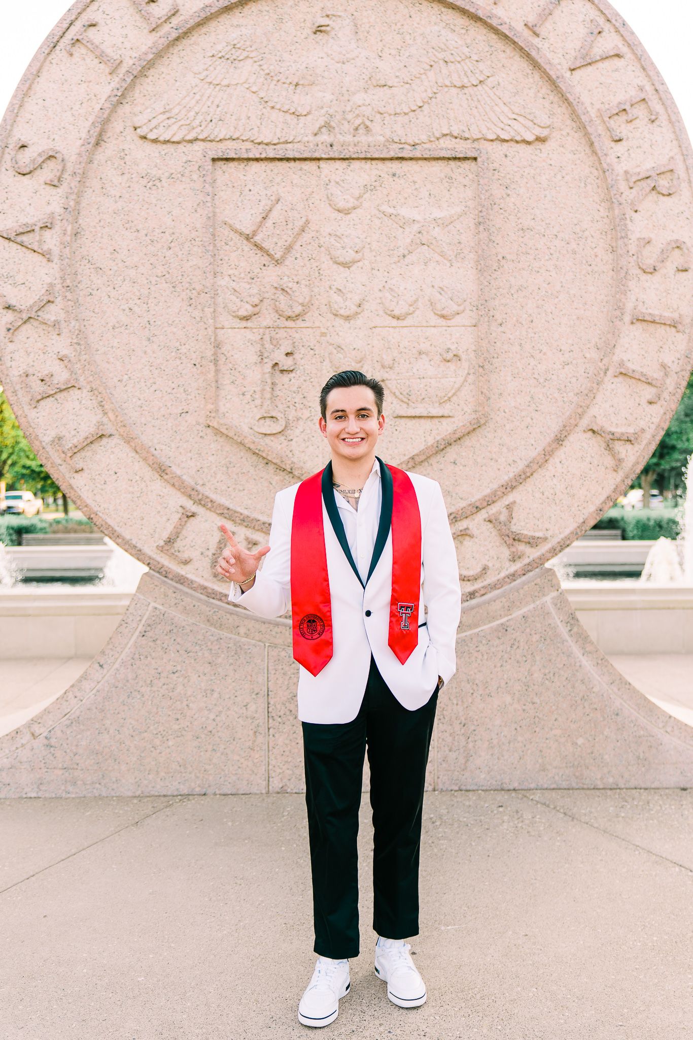 Graduate in white and red academic regalia poses against a stone wall with carved details.