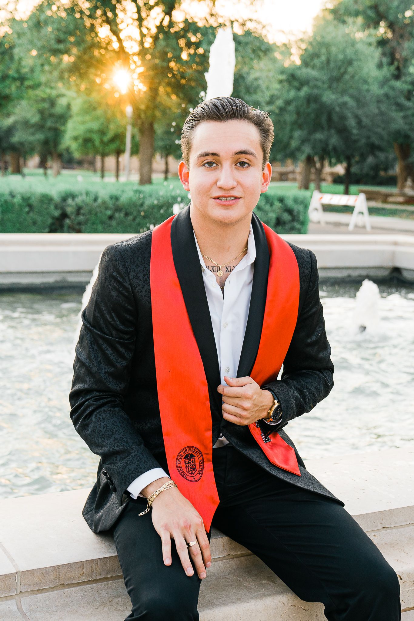 Outdoor graduation portrait series at sunset near a pond wearing black suit and orange stole.