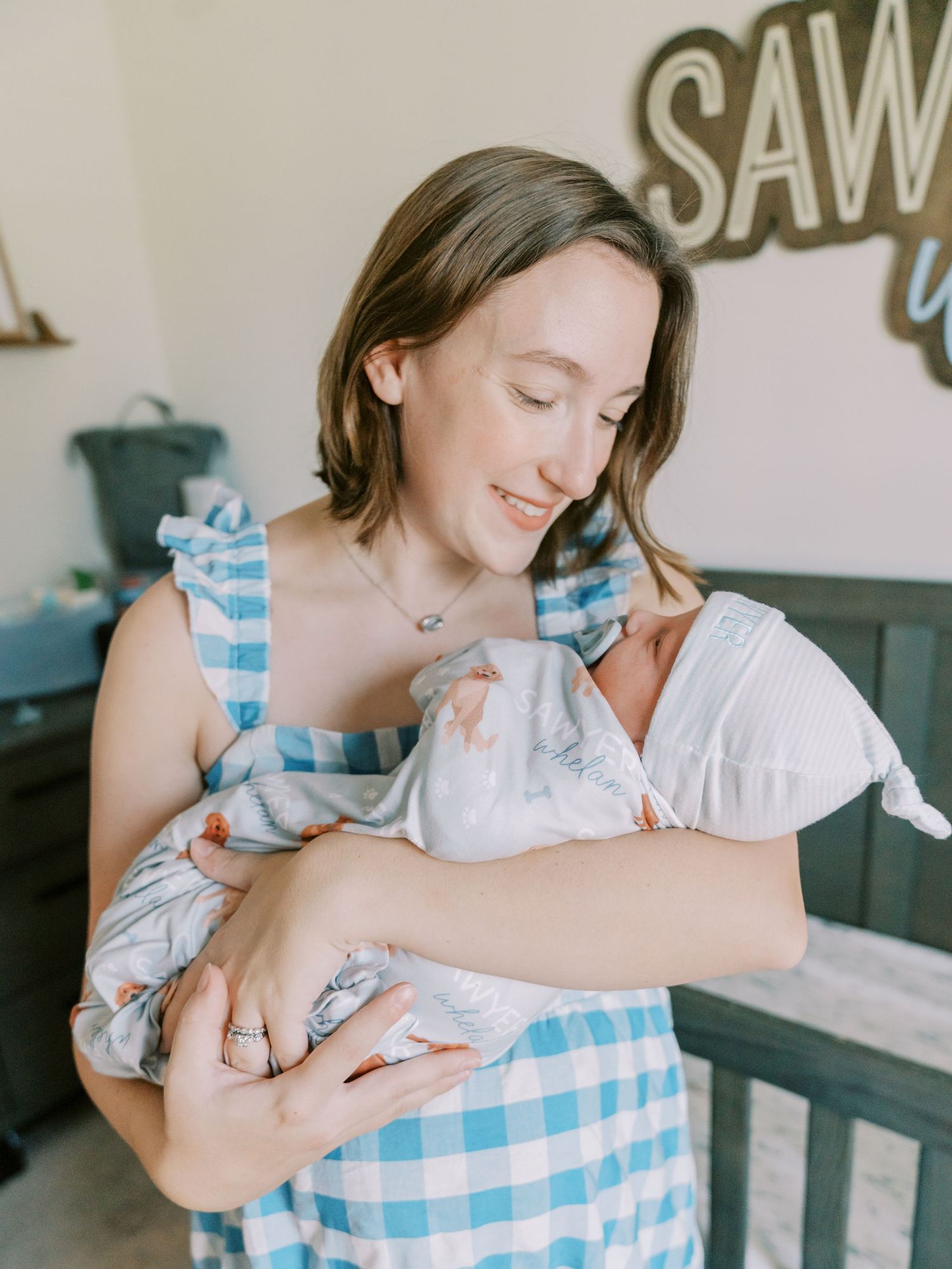 Mother in blue gingham dress holds newborn in white clothing.