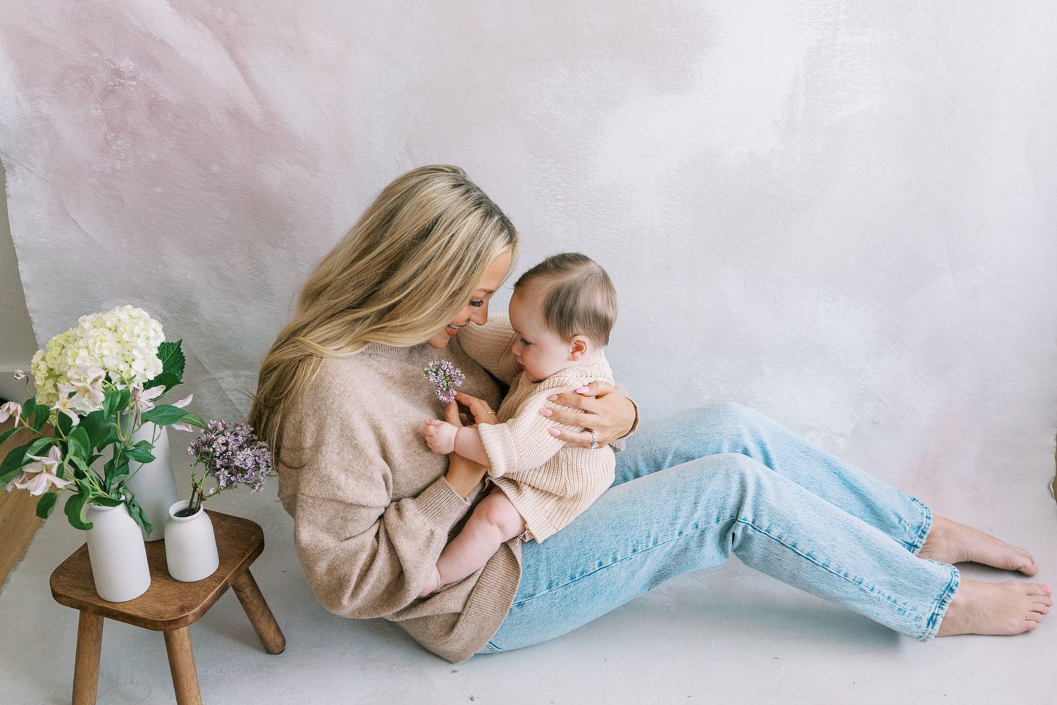 Mother and baby in soft neutral tones lounging together on light pink backdrop.