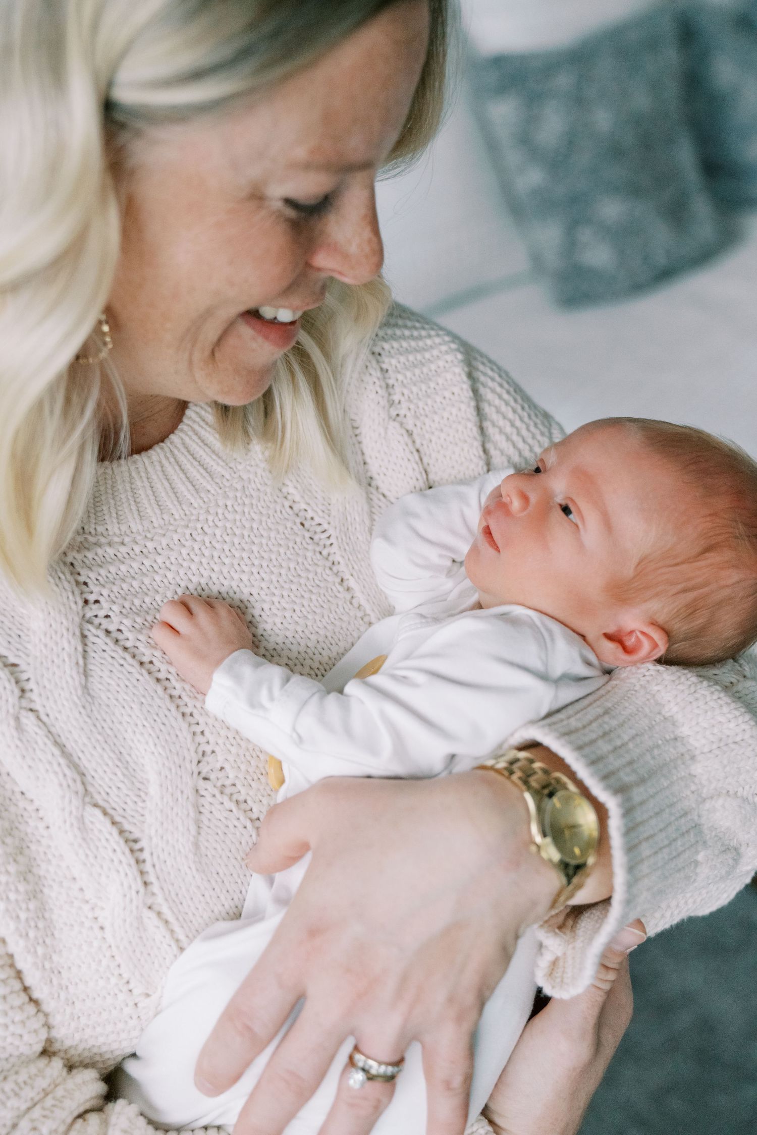 Mother in white sweater gazing lovingly at newborn baby in white outfit.