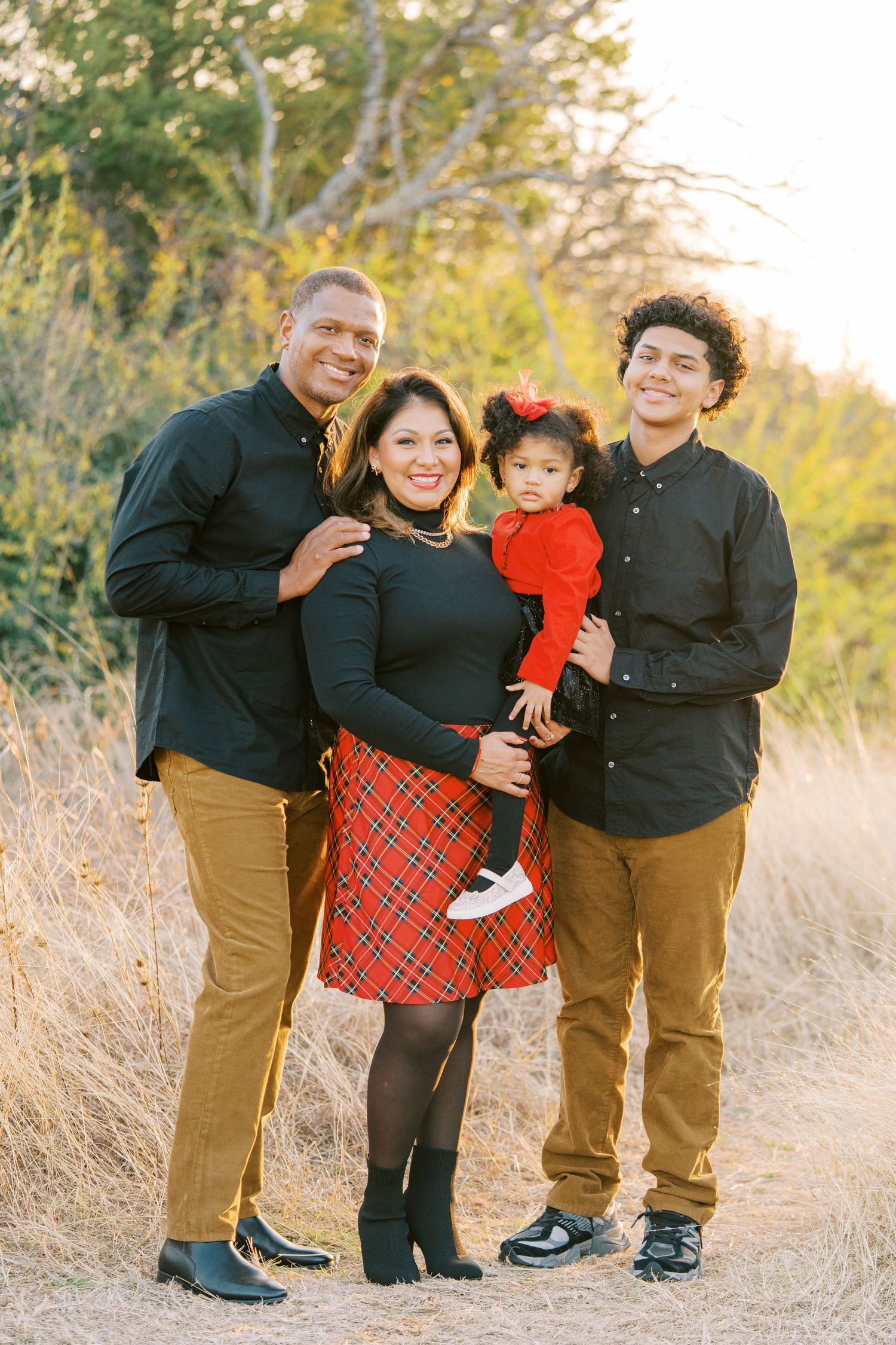 Family of four wearing coordinated black outfits poses together in a natural outdoor setting at sunset.