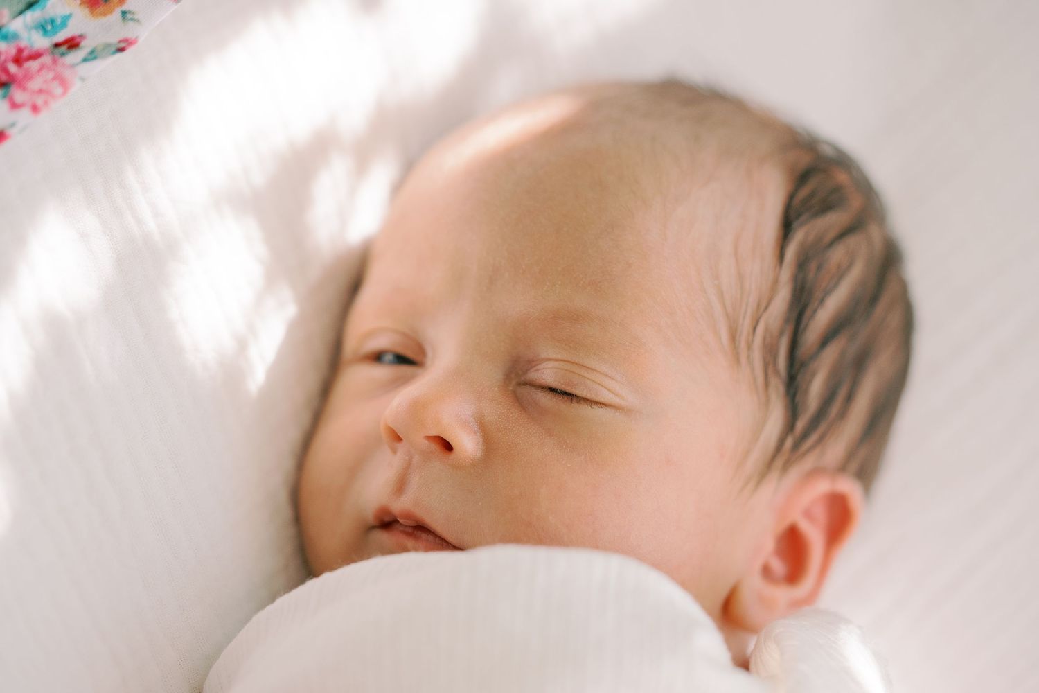 A sleeping infant rests peacefully on white bedding in soft natural light.