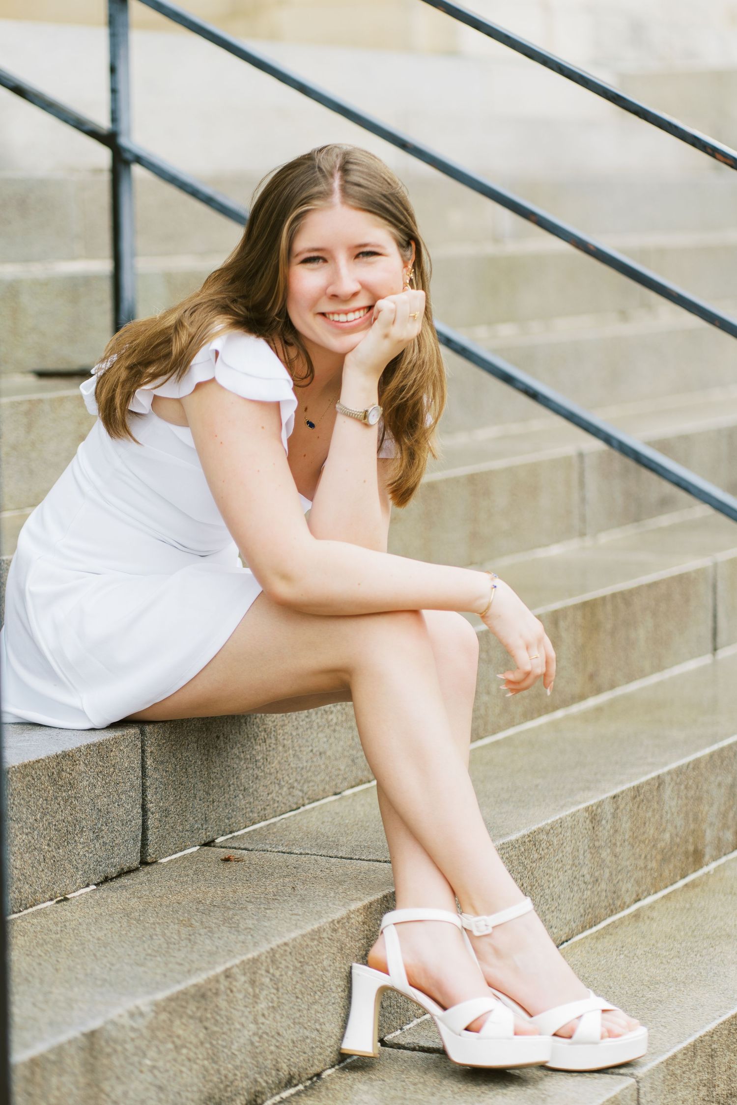 A person in a white dress sits casually on concrete steps wearing platform sandals on a sunny day.