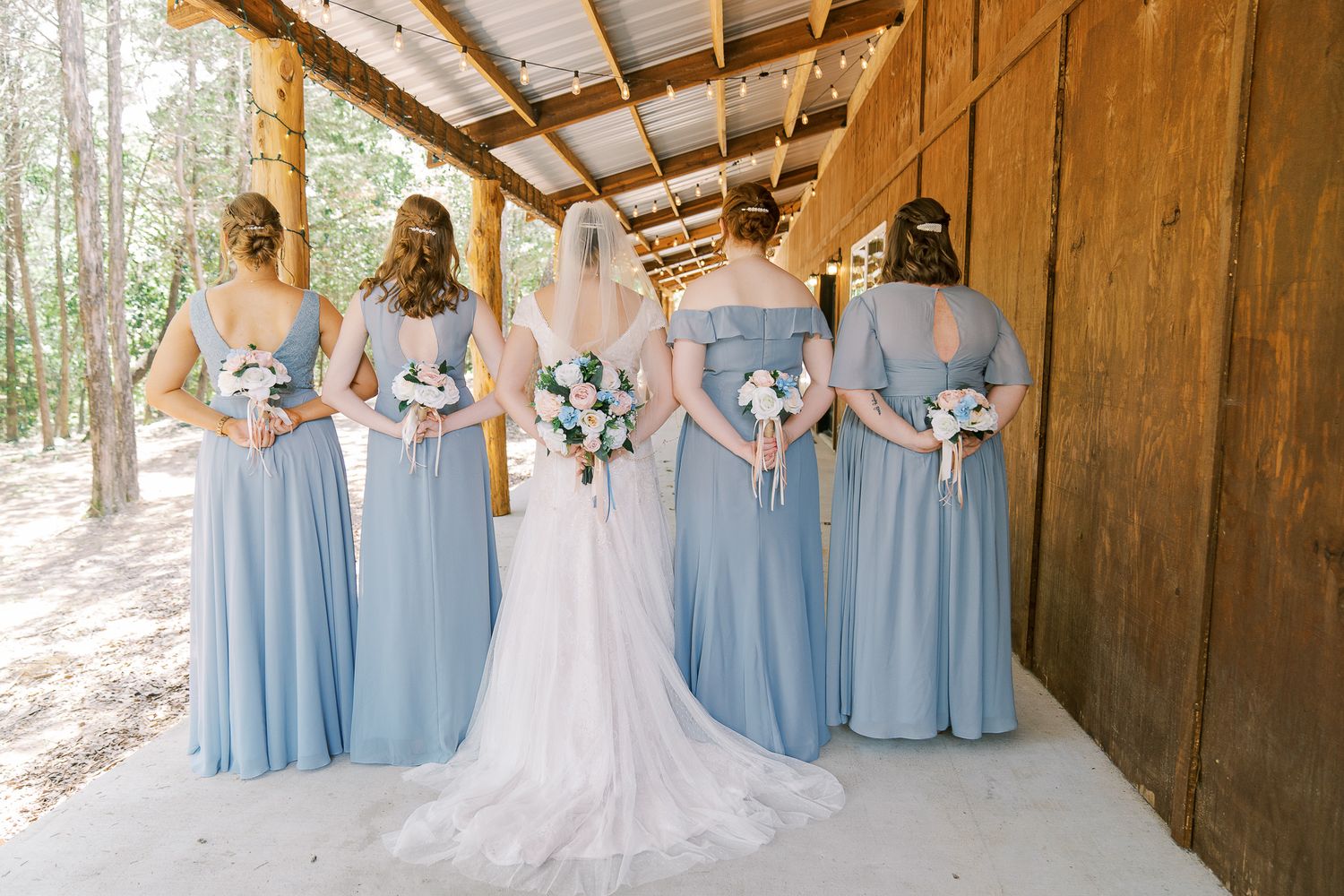 Wedding party poses in rustic wooden barn with bridesmaids in light blue dresses and white bridal gown.