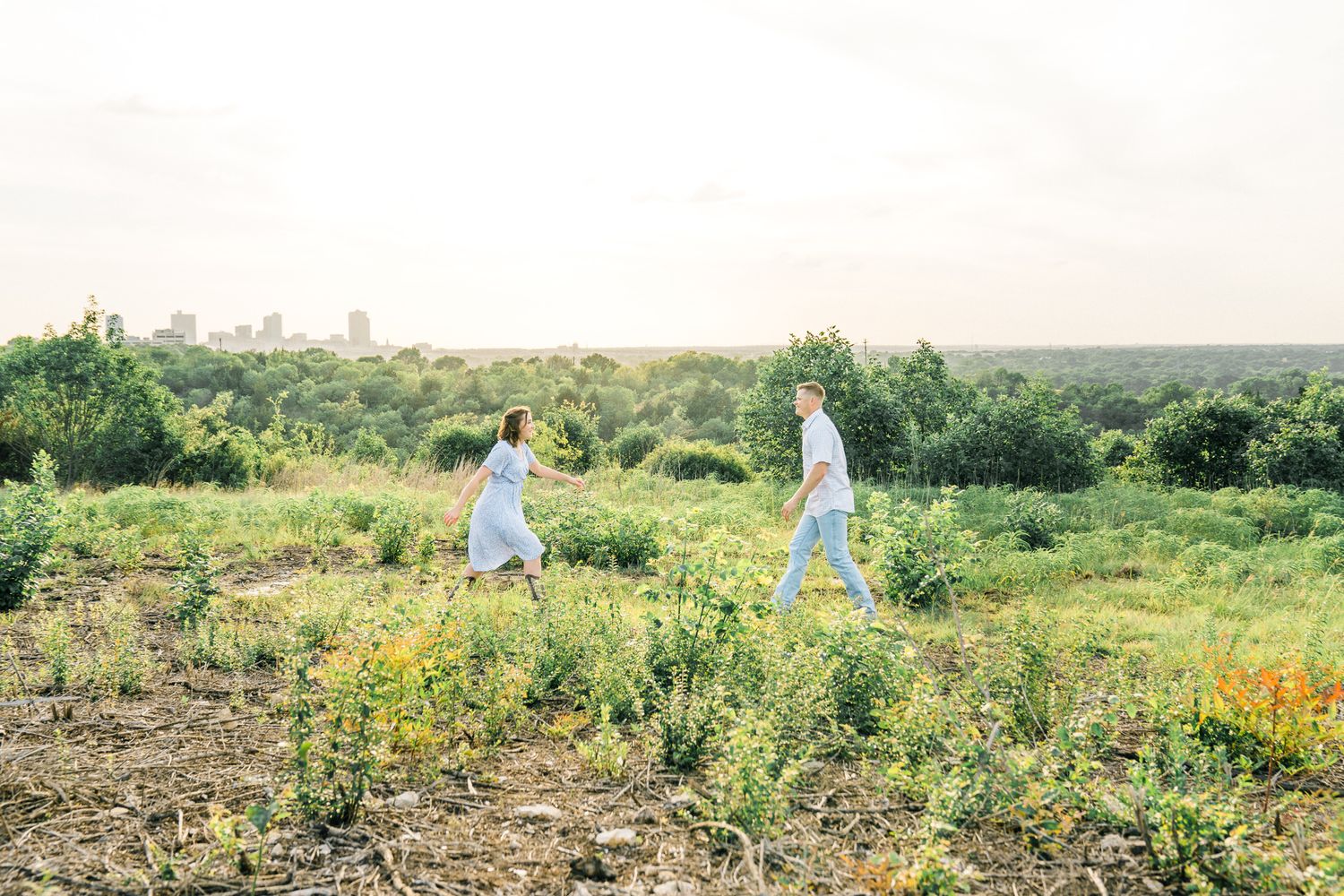 Two people explore a flowering meadow with a distant city skyline visible on the horizon.