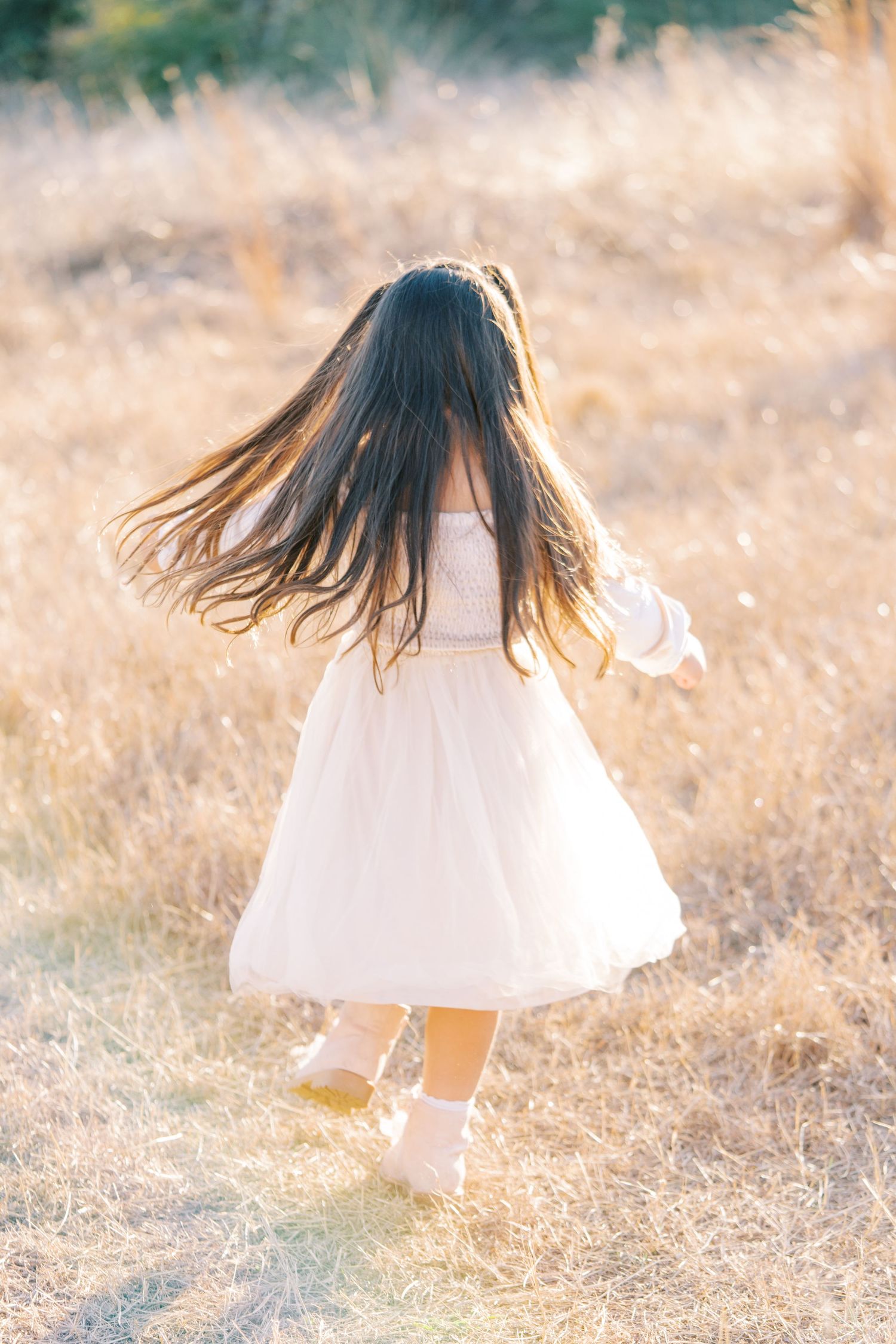 A young girl in a white dress twirls and dances in a sunlit meadow during golden hour.
