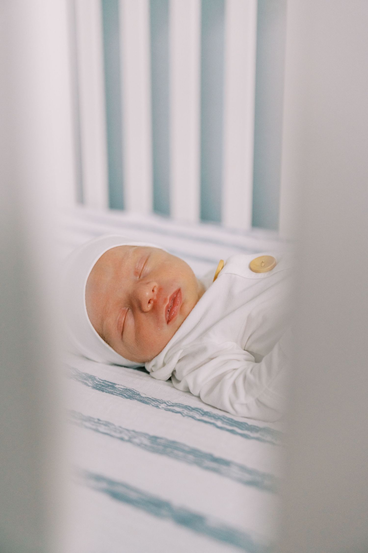 Newborn sleeping peacefully in a white crib with fitted sheets.