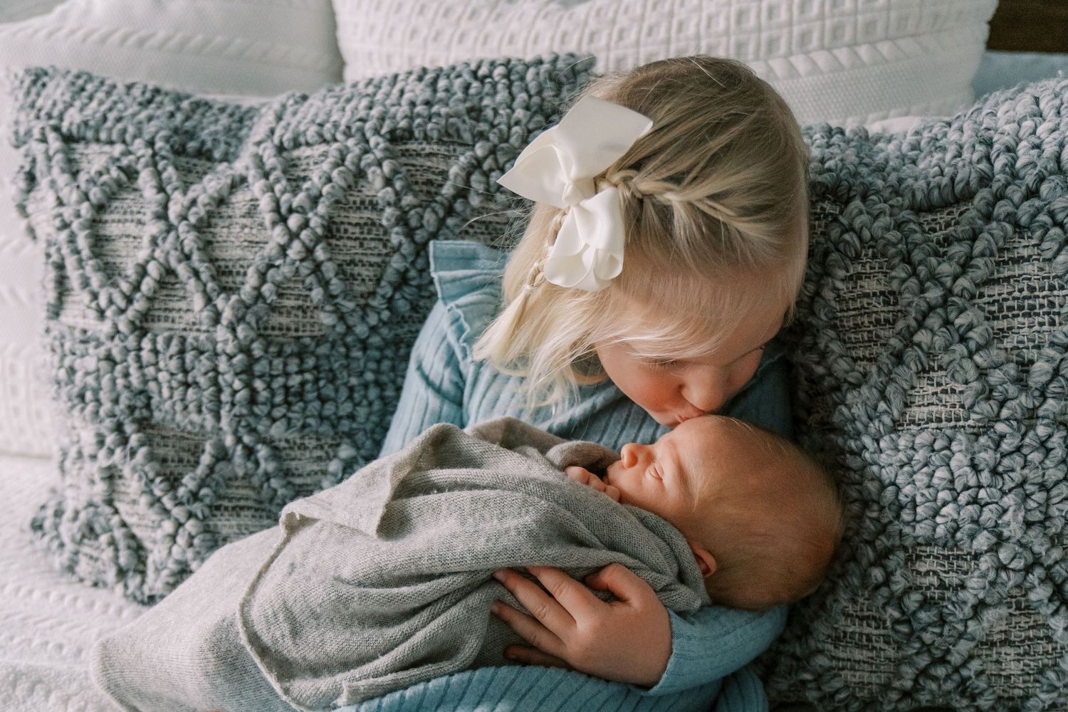 Two siblings sharing a tender moment on a textured gray pillow.