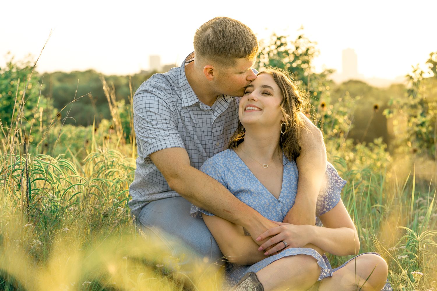 A tender moment shared between a couple sitting in a grassy field at sunset with warm golden light.