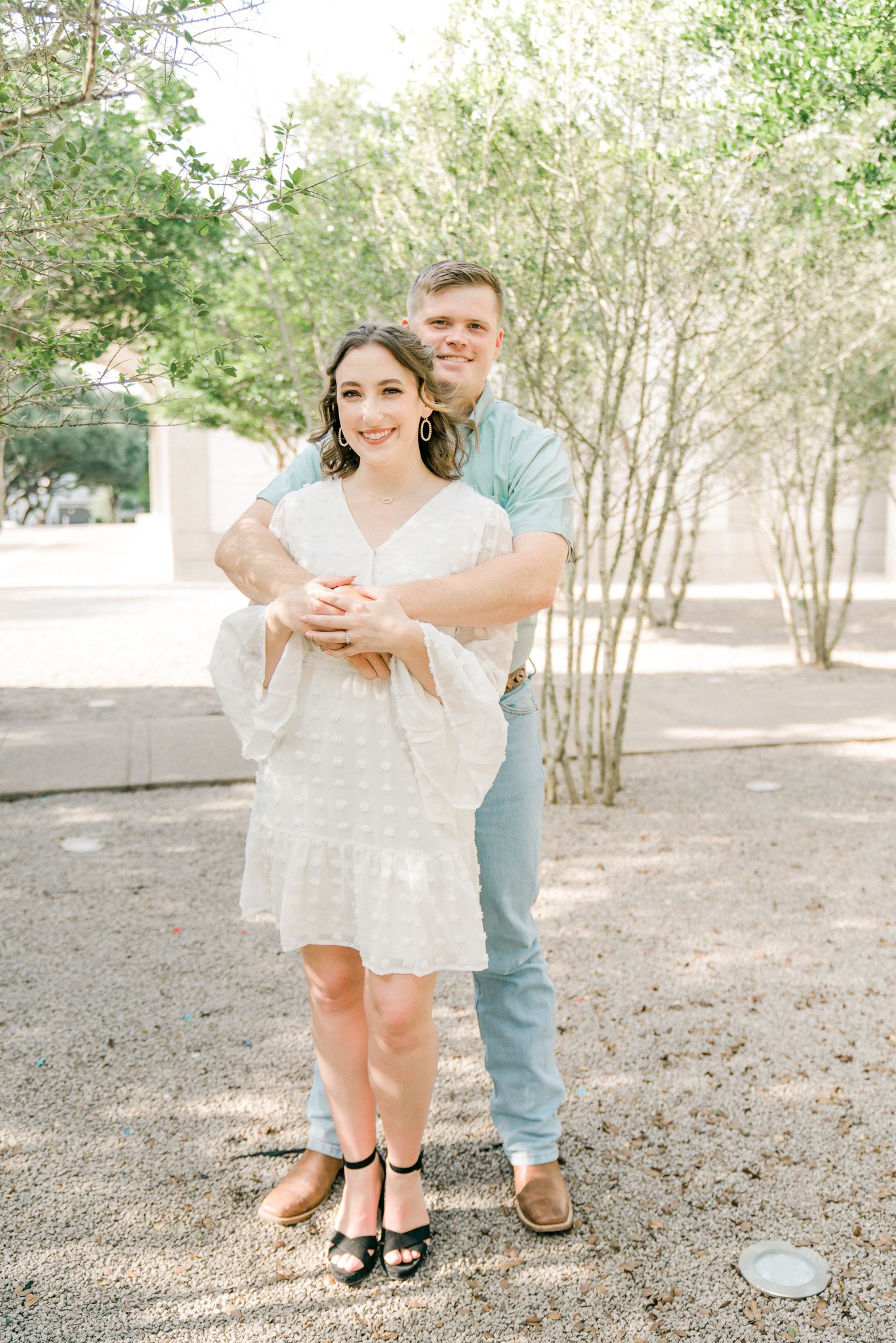 Couple dancing playfully together in a park setting with trees in the background.