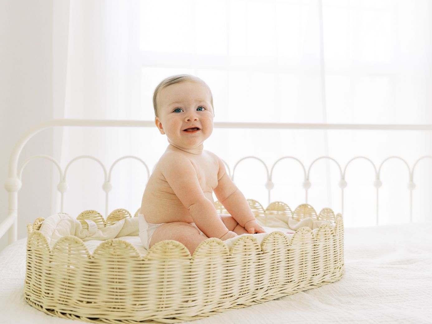 Happy baby sitting in a decorative woven basket against a white background.