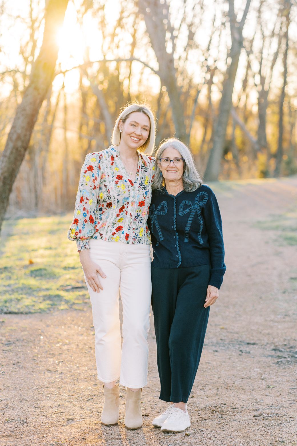 Two people walking together on a dirt path at sunset with golden sunlight filtering through trees in the background.