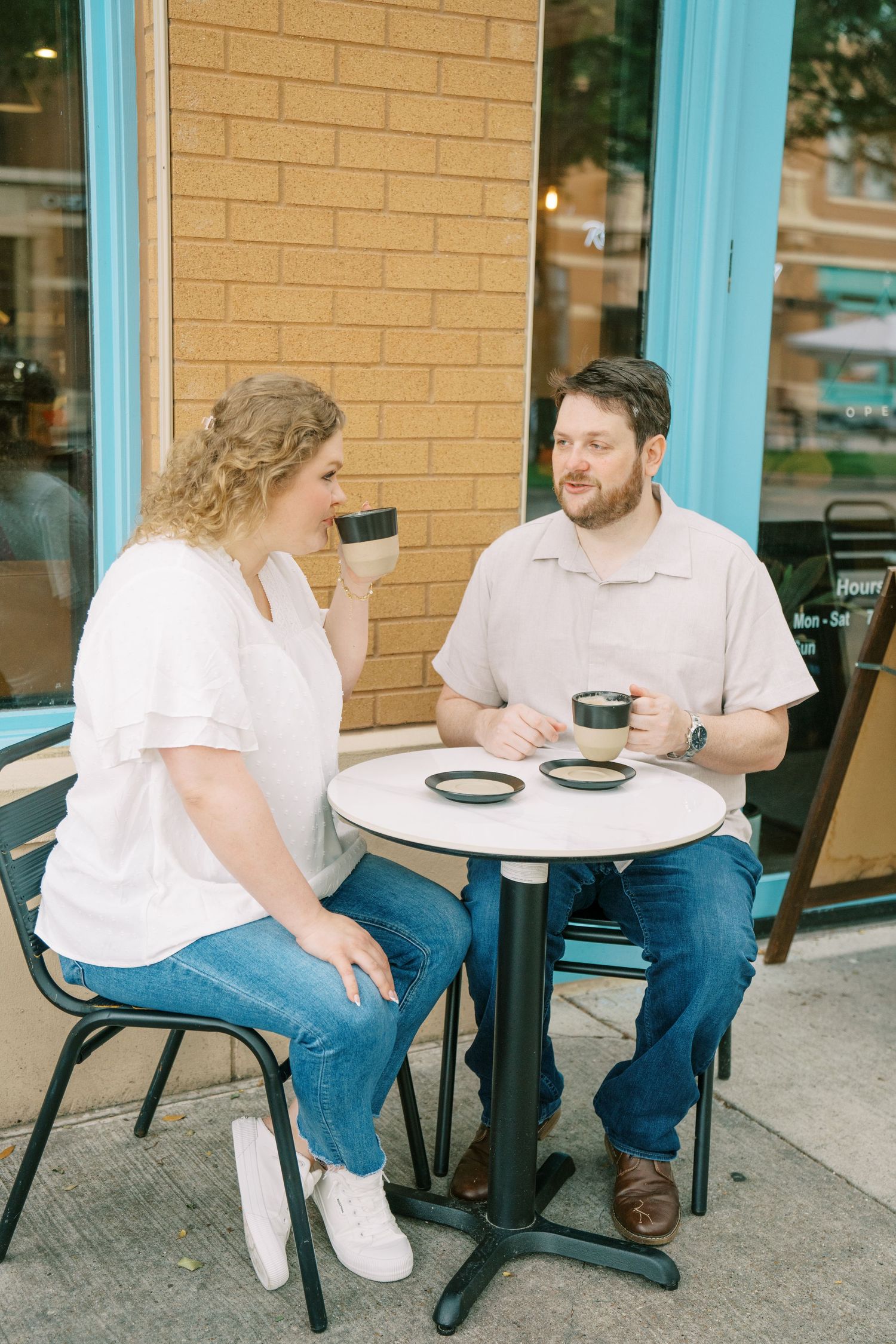 Couple enjoying coffee together at an outdoor cafe table on a sunny day, smiling and chatting.