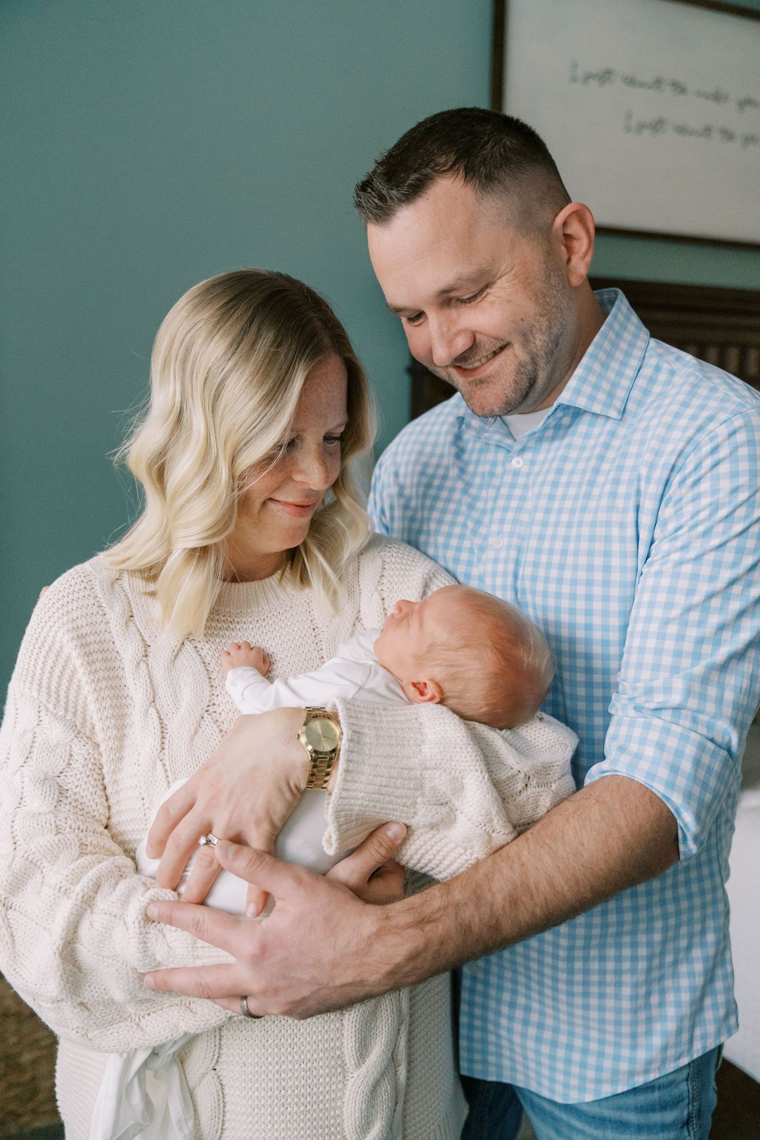 Parents in white and blue outfits holding their newborn baby in a nursery.