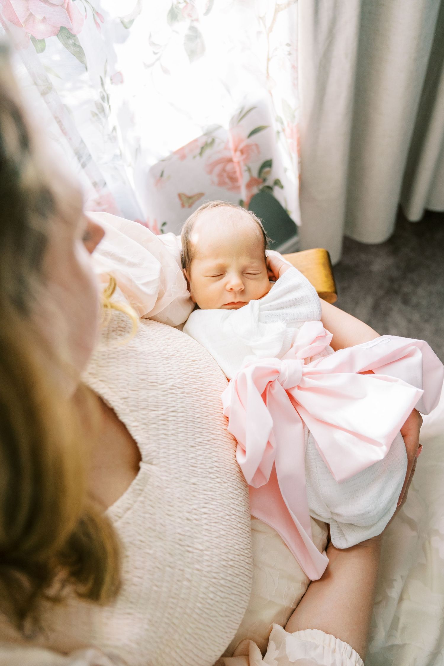 A sleeping newborn wrapped in pink blankets rests peacefully in soft window light.