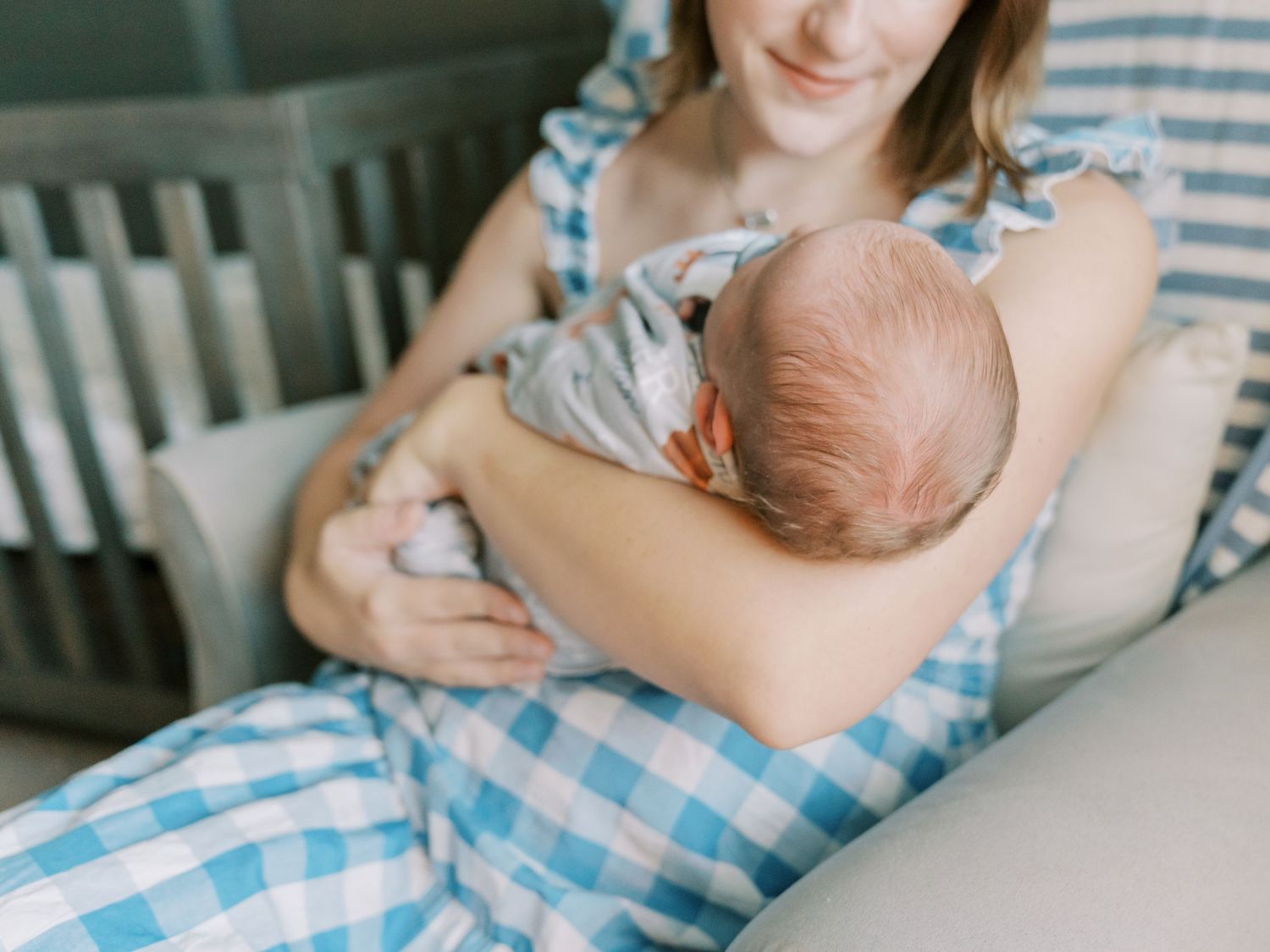 A parent holds and nurses a baby while sitting on a blue and white checkered blanket.