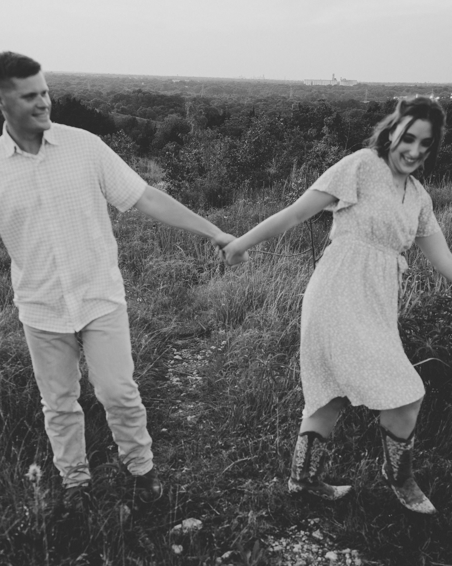 Group of people walking through a tall grass meadow wearing white clothing in black and white photography.