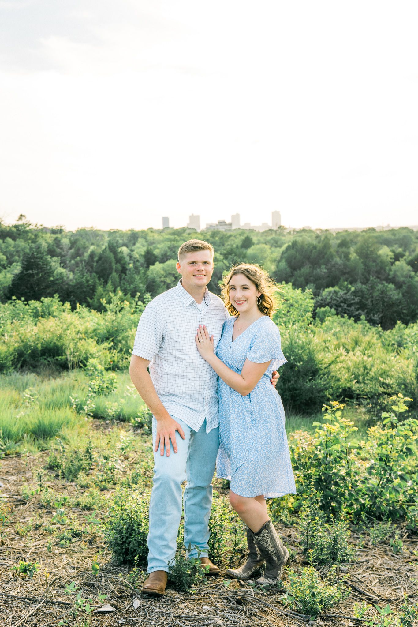 A couple poses against a scenic cityscape backdrop with lush greenery in the foreground.