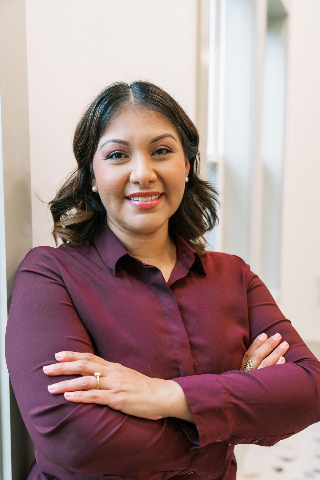 Professional headshot of someone in a burgundy button-up shirt standing with arms crossed and warm smile.