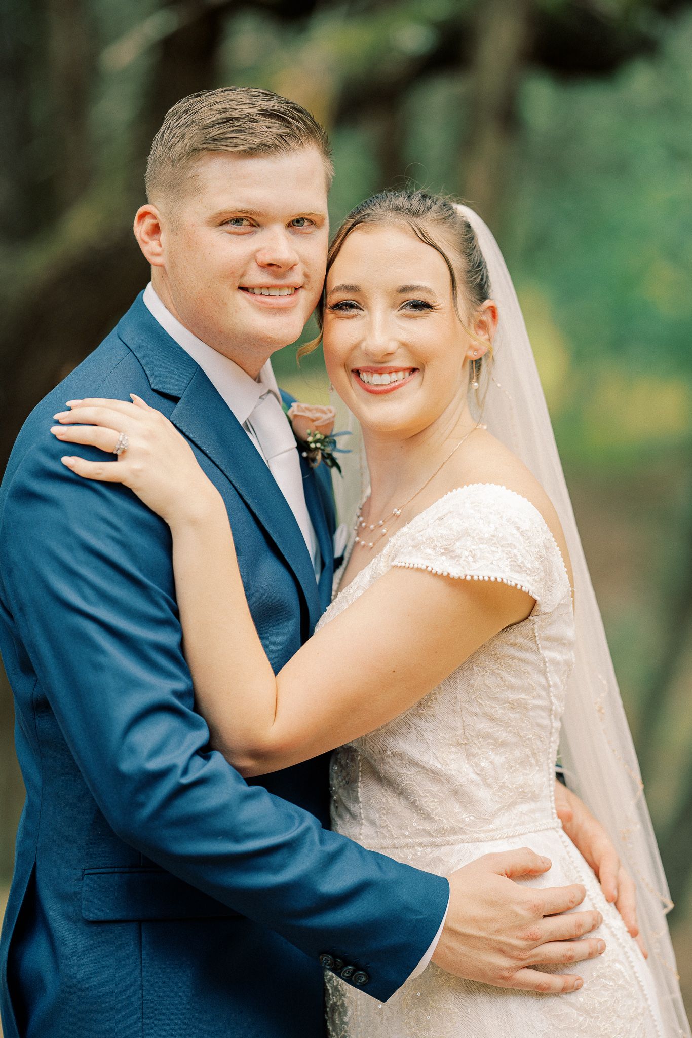 A romantic wedding portrait series showing a couple in navy suit and white lace dress embracing outdoors.