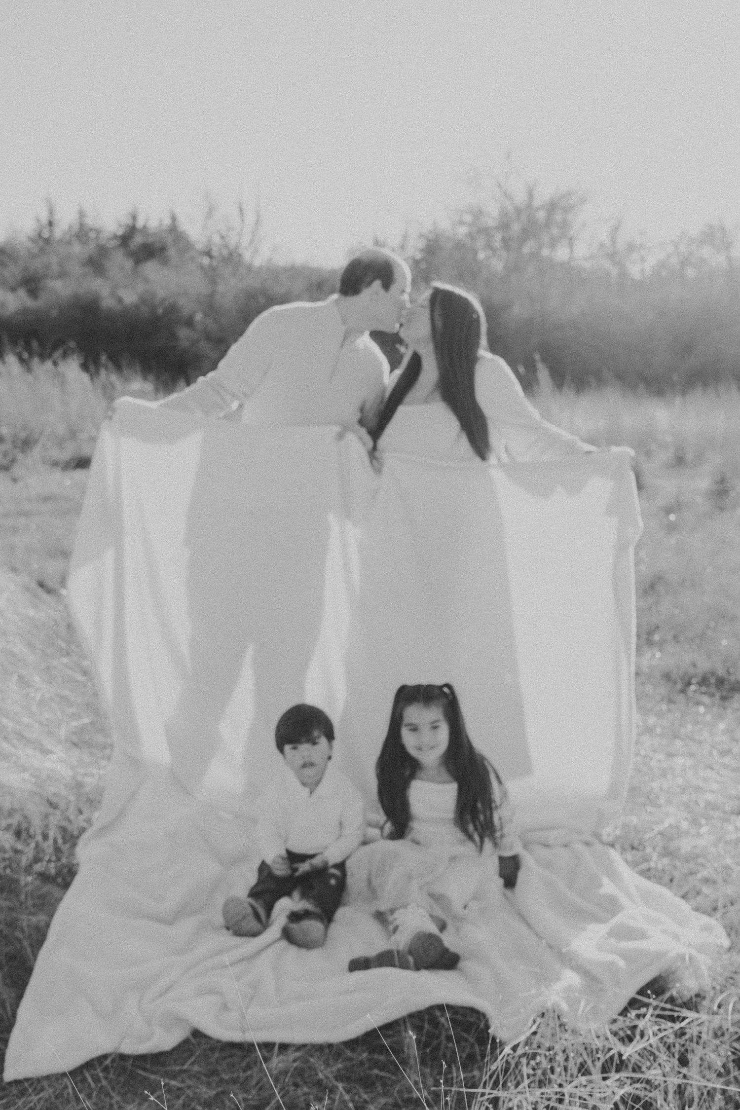 Black and white photo series showing children playing with white sheets in a grassy outdoor setting.