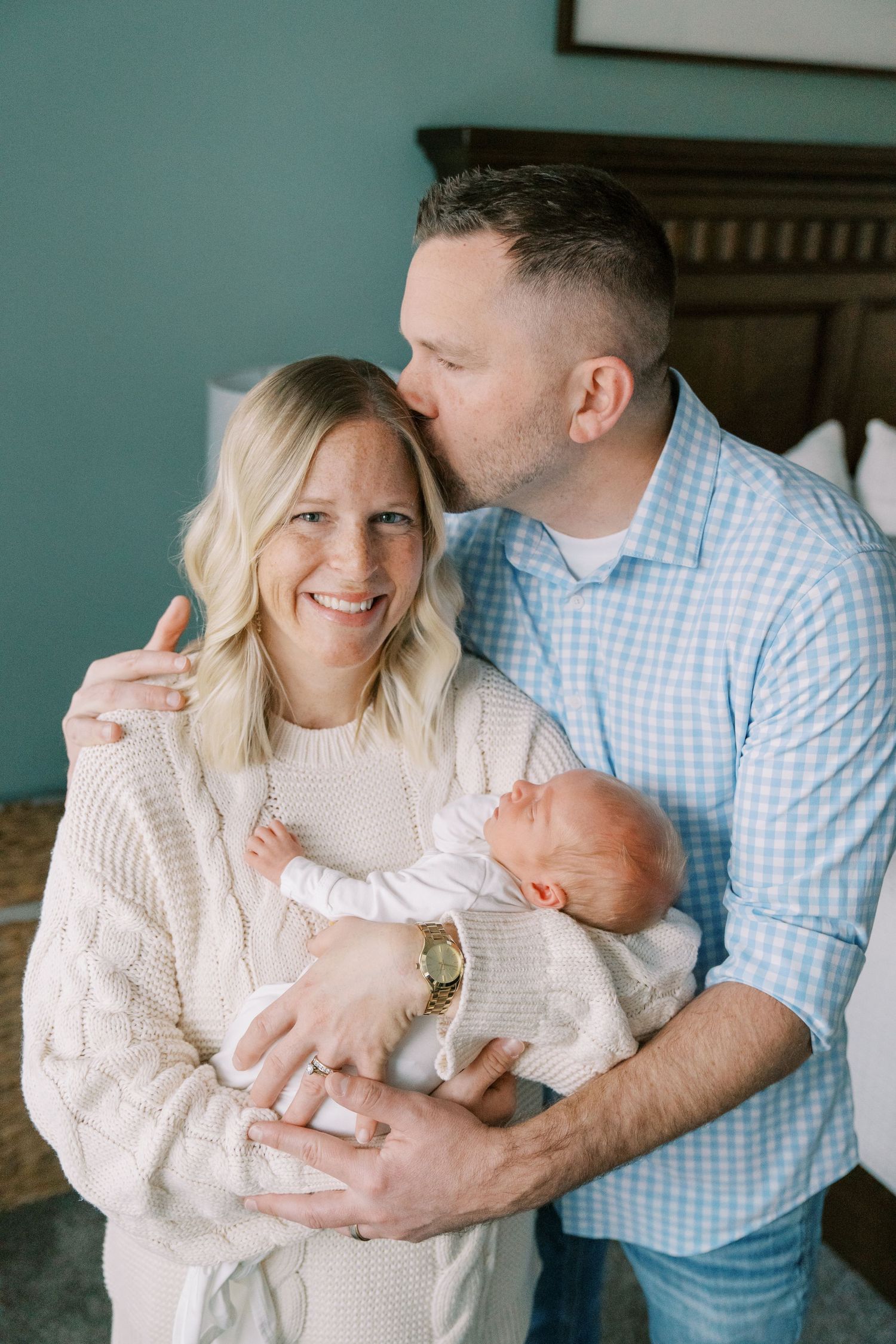 New family shares intimate moment together while holding their newborn baby in white knit sweater.