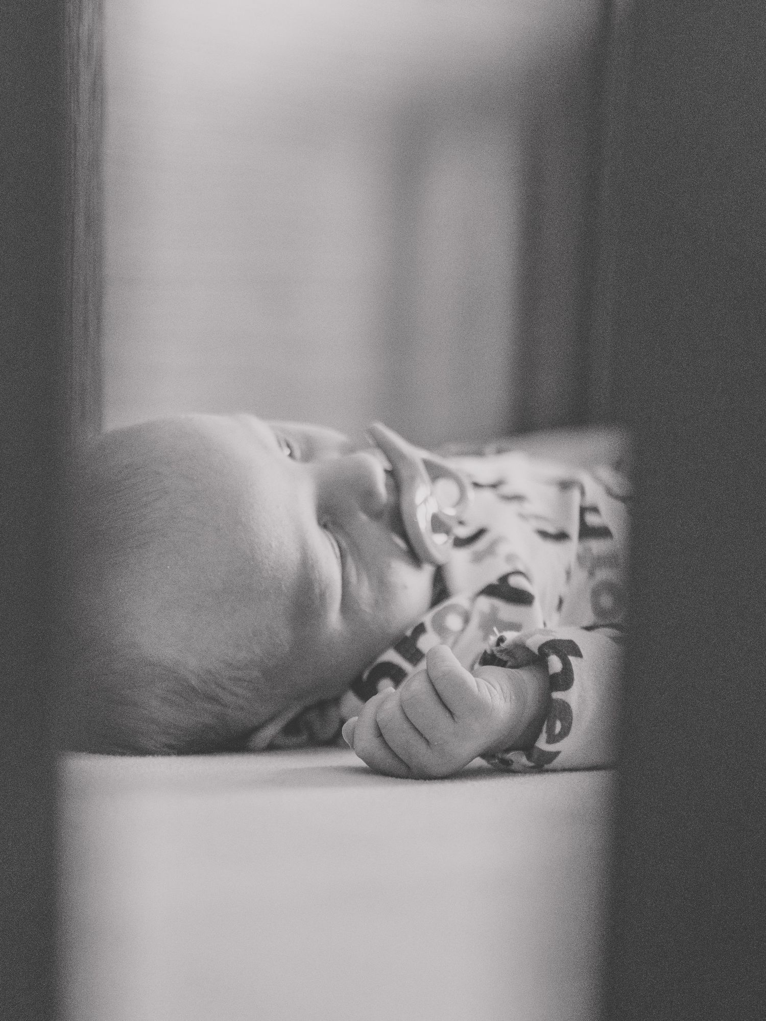 Black and white photo of sleeping infant through crib slats.