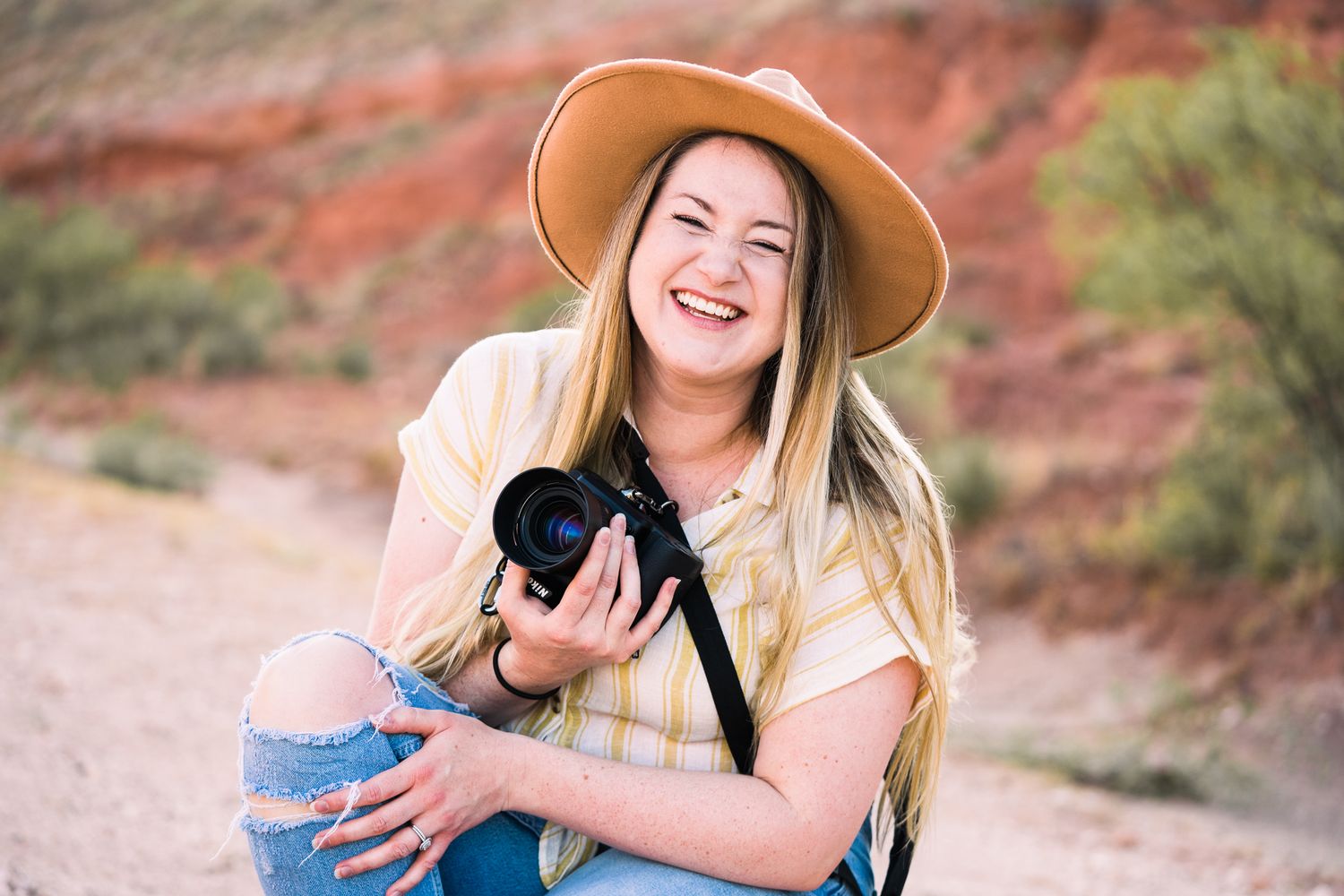 Woman in hat and striped top smiling while exploring desert landscape.