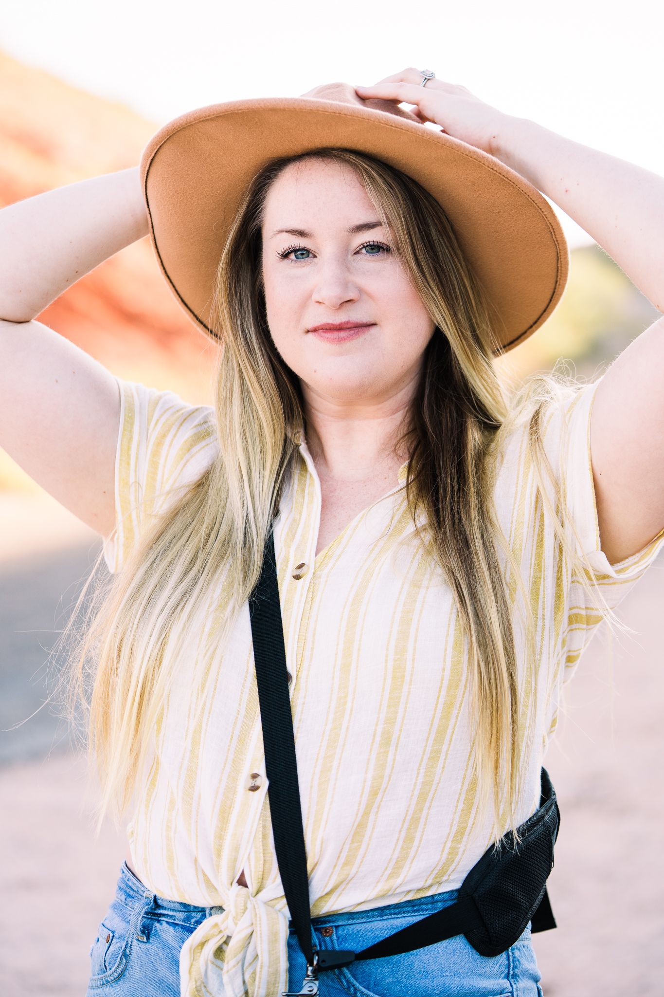 Person in a wide brim hat and striped shirt posing against a soft sunset background.