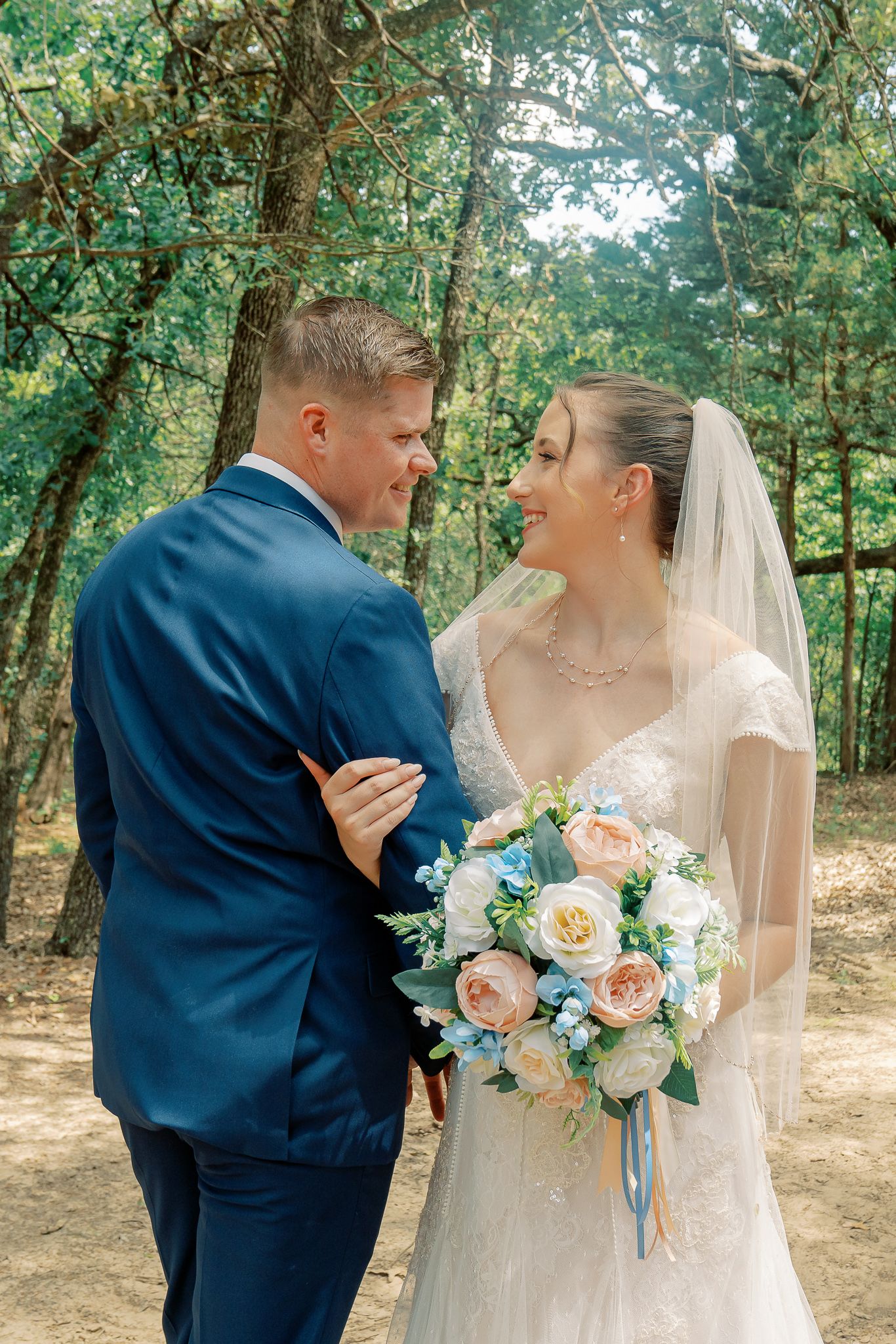 A romantic wedding couple shares tender moments in a wooded outdoor setting with soft natural lighting.