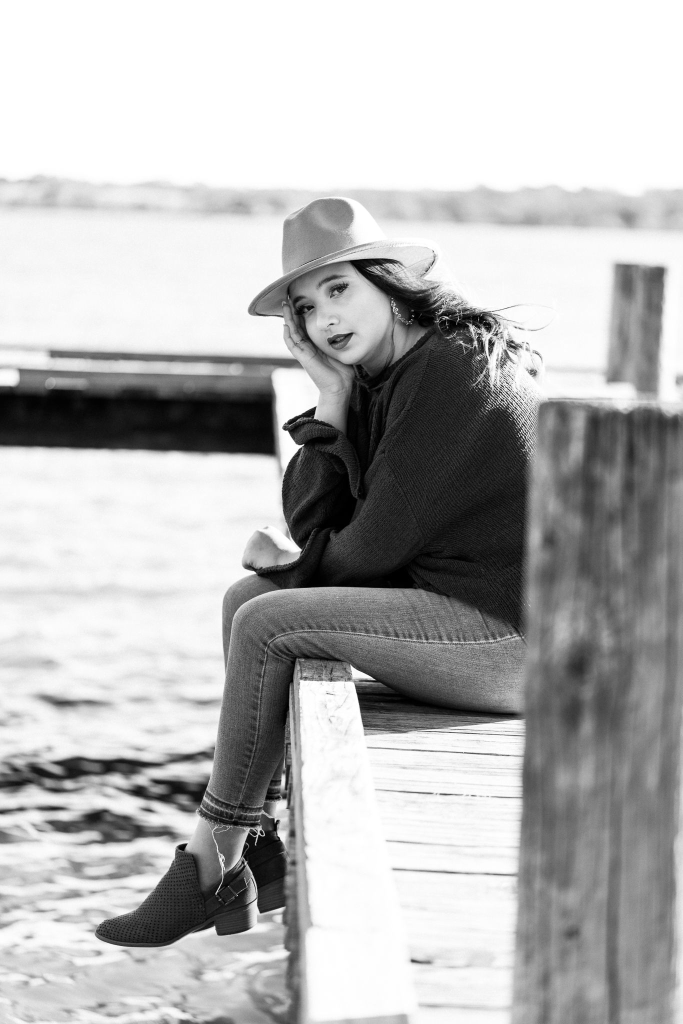Black and white portrait of someone in casual attire sitting on wooden dock posts.