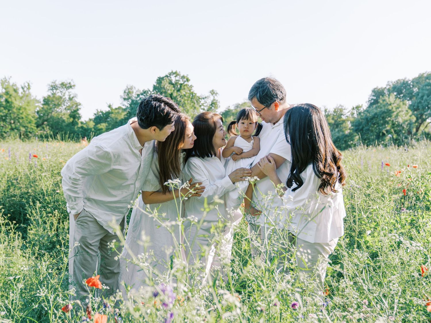 Family in white outfits gathering together in a wildflower meadow on a sunny day.