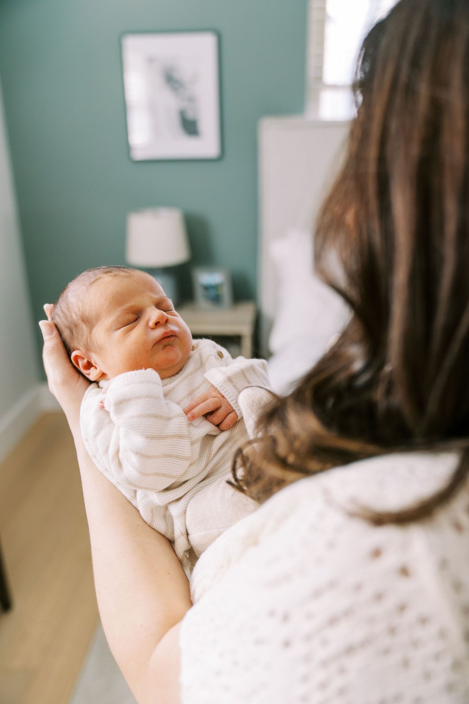 A sleeping newborn baby wearing white clothing rests peacefully in someone's arms in a nursery setting.