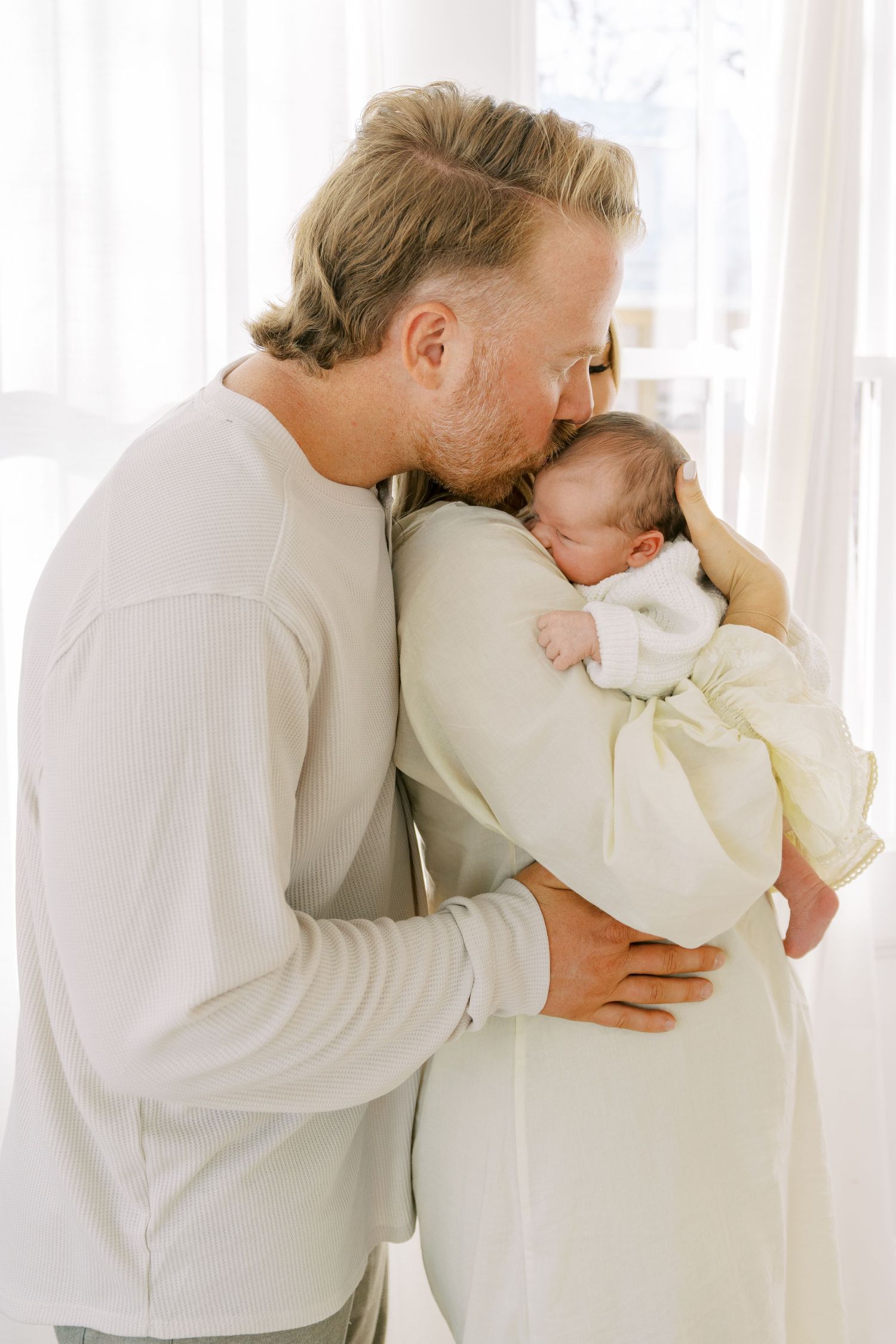 Intimate family moments captured in white clothing against bright interior backdrop.